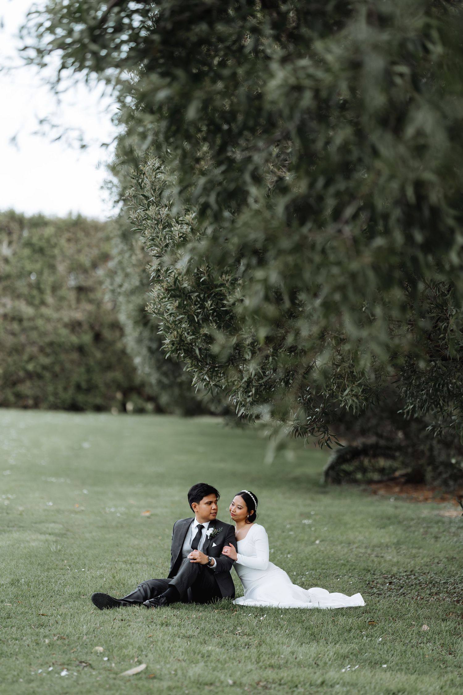 Couple sitting on grass having intimate moment under overhanging tree branches.