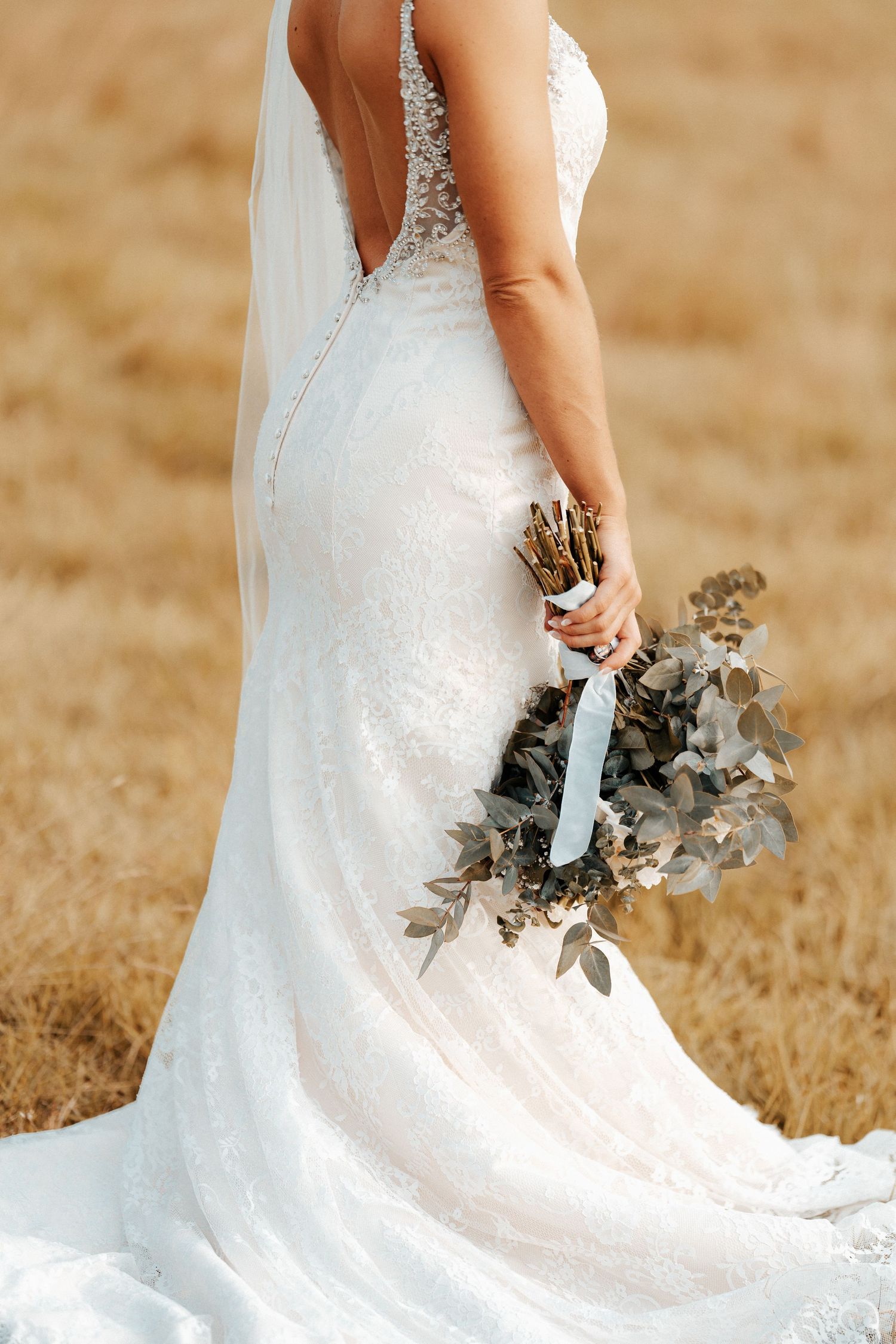 An elegant white lace wedding dress with a flowing train photographed in a golden field.