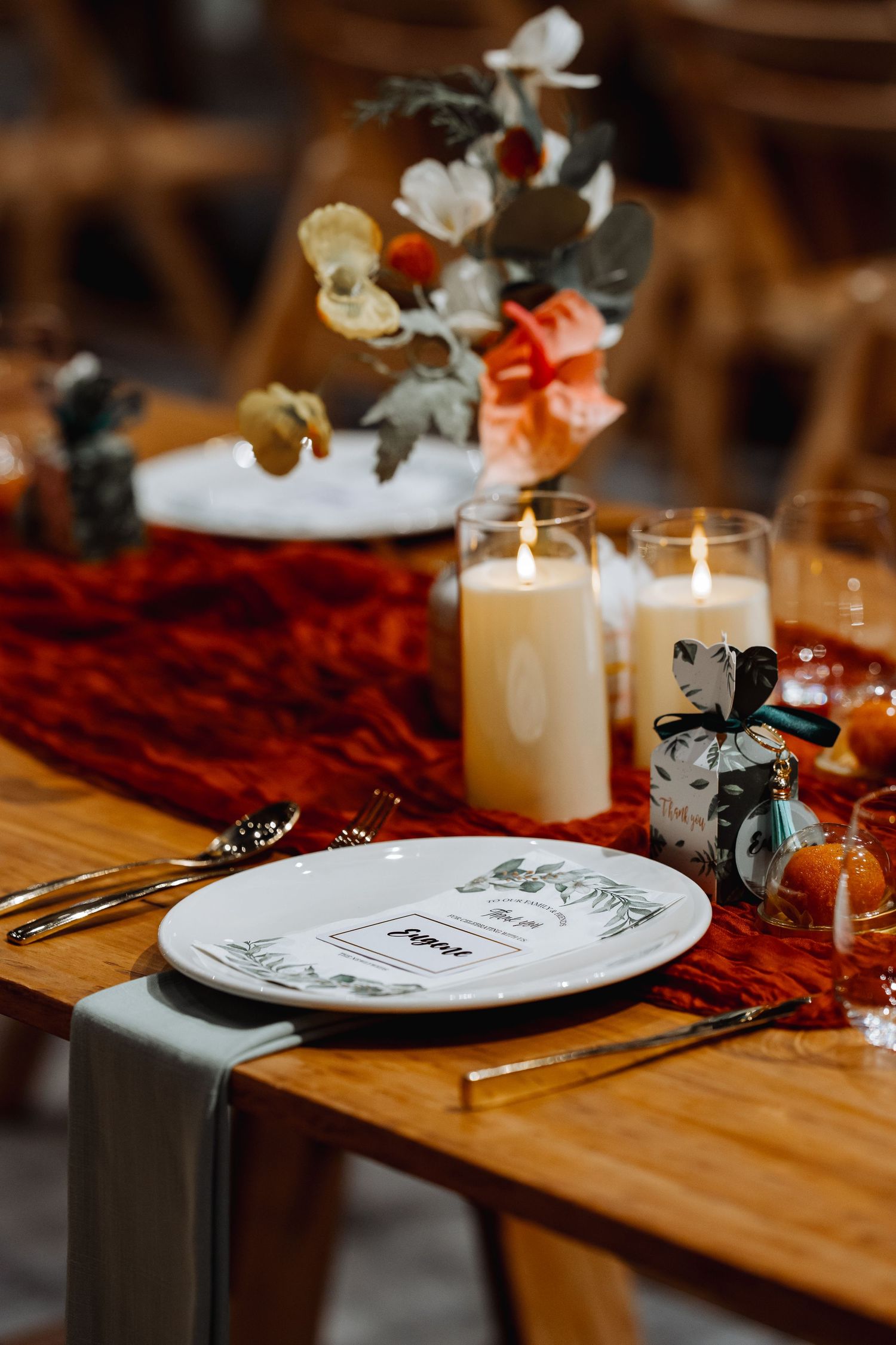Wedding reception table setting with candles, flowers and place cards in warm lighting.