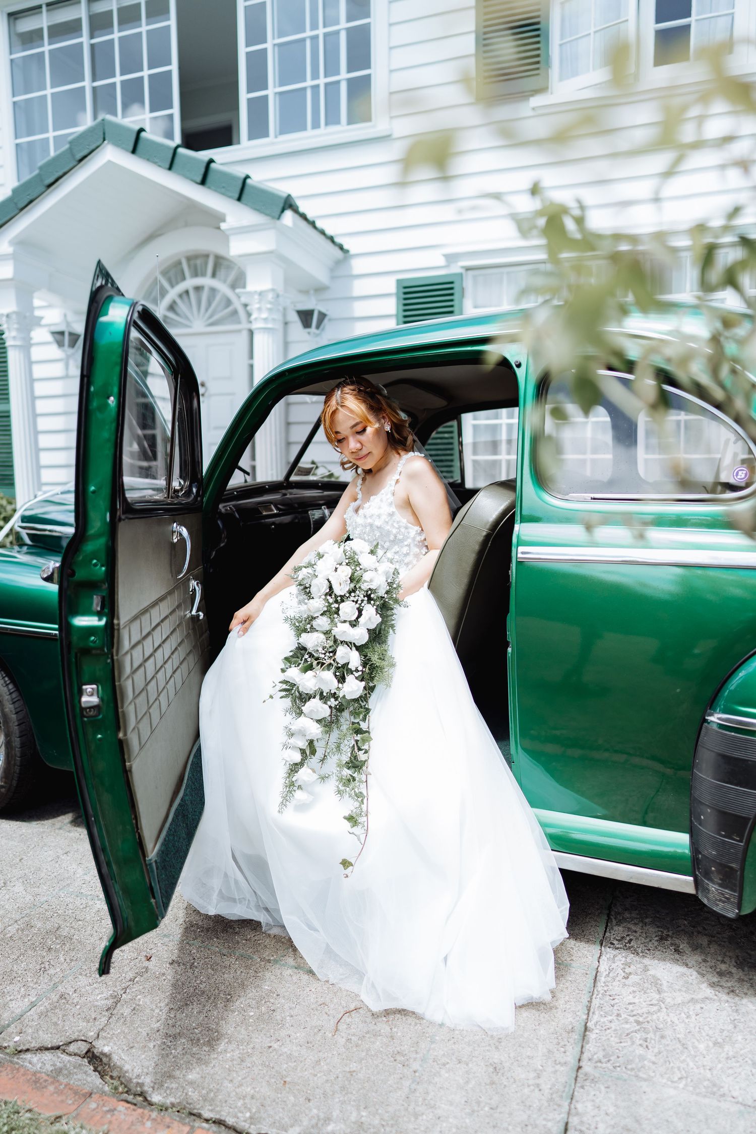 A bride in a white wedding dress enters a vintage green car in a series of sequential photos.