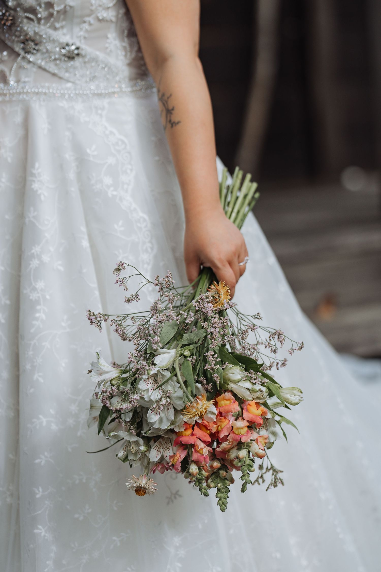 Close-up of bride holding delicate bouquet with coral flowers against white lace dress.