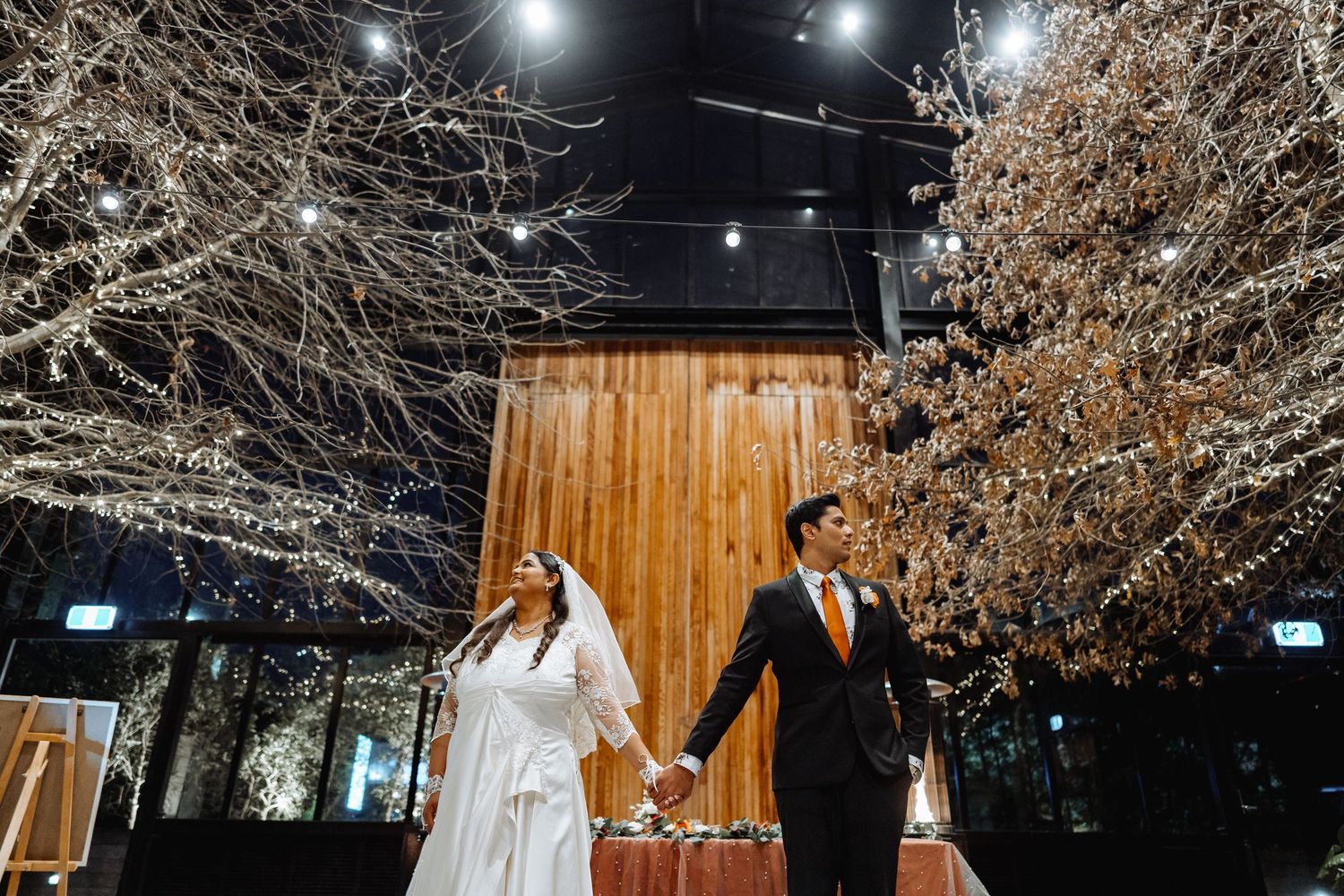 An outdoor wedding reception setup at night with twinkling lights and bare winter trees.