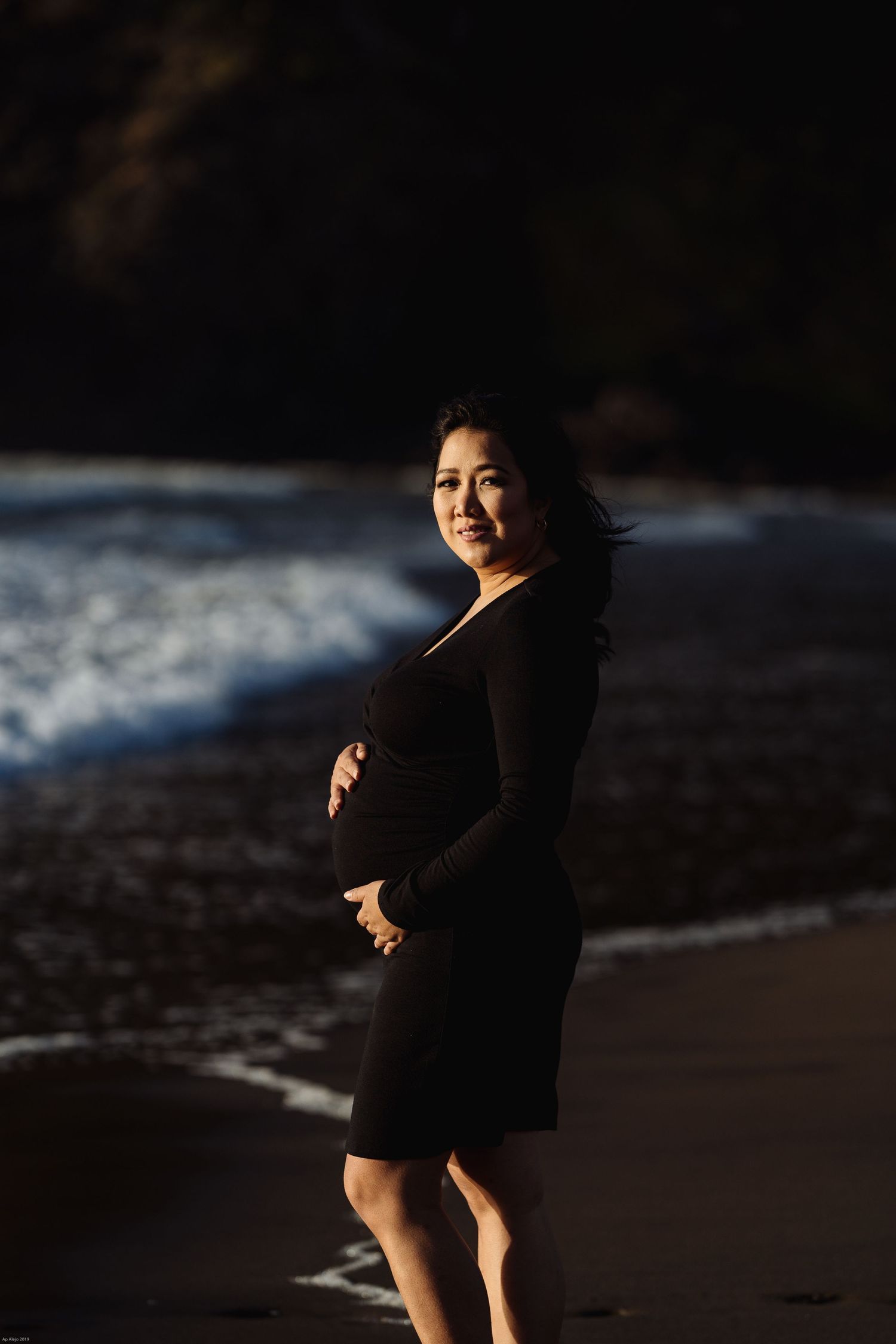 Dramatic beach portrait in dark tones with ocean waves in background.