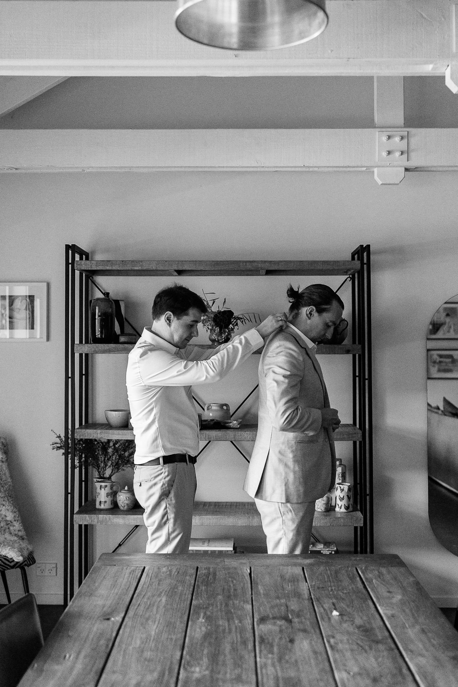 Black and white sequence showing two people in white attire interacting near a wooden table.