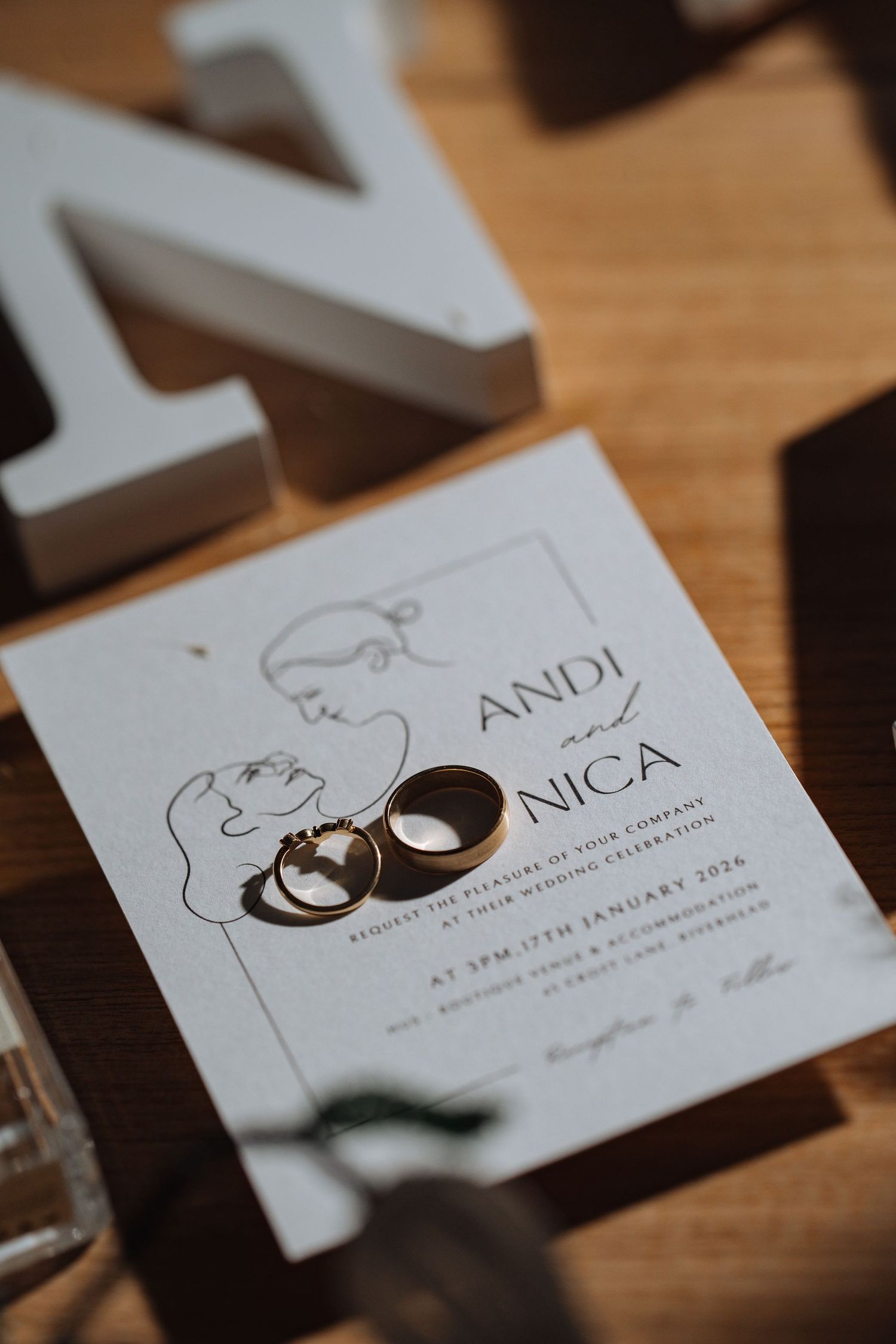 Close-up of wedding invitation cards with minimalist design and rings creating dramatic shadows.