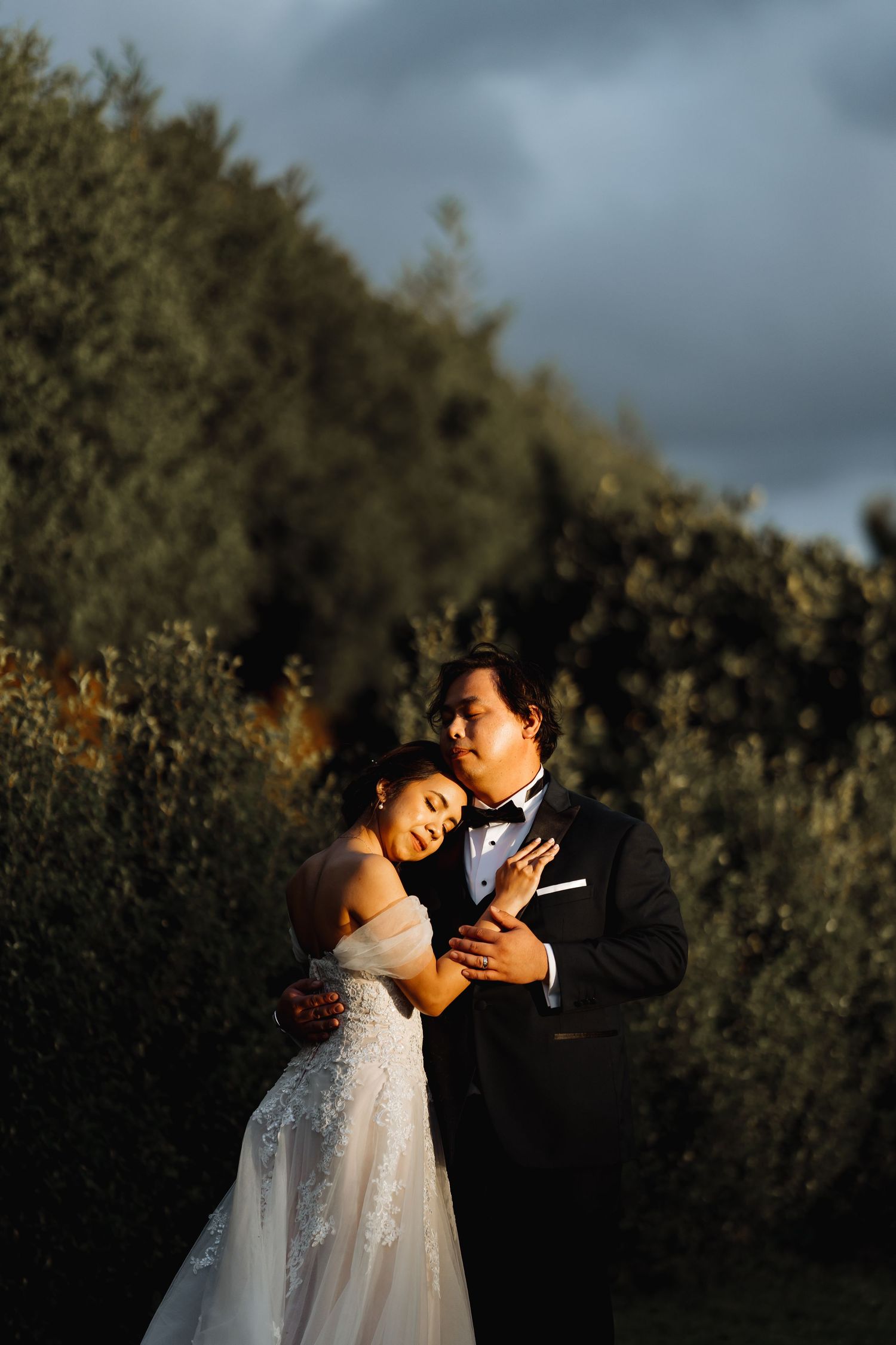 Sunset wedding photos with dramatic lighting showing couple embracing in garden setting.