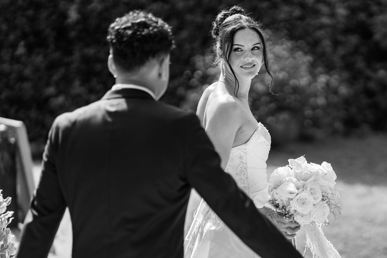 Black and white outdoor wedding ceremony photograph with natural garden setting.