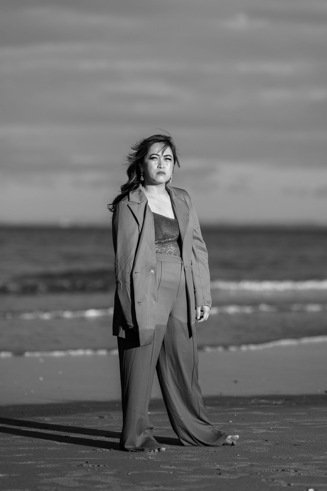 Artistic black and white beach portrait showing person lying on sand with dramatic lighting.