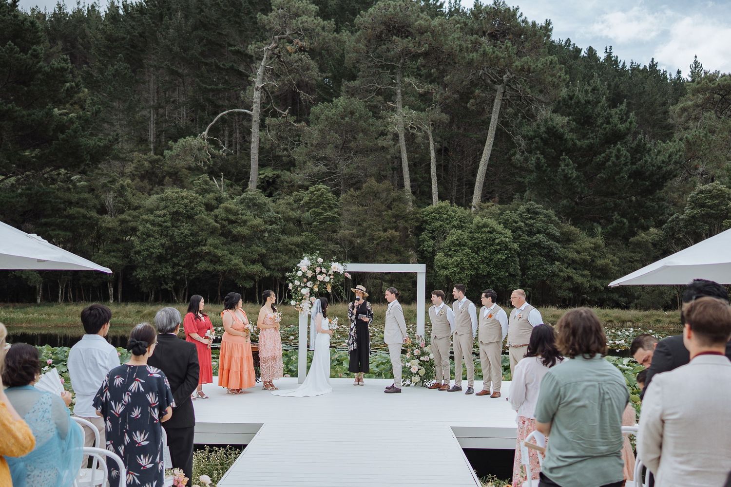 Wide shot of wedding guests gathered outdoors with forest backdrop.
