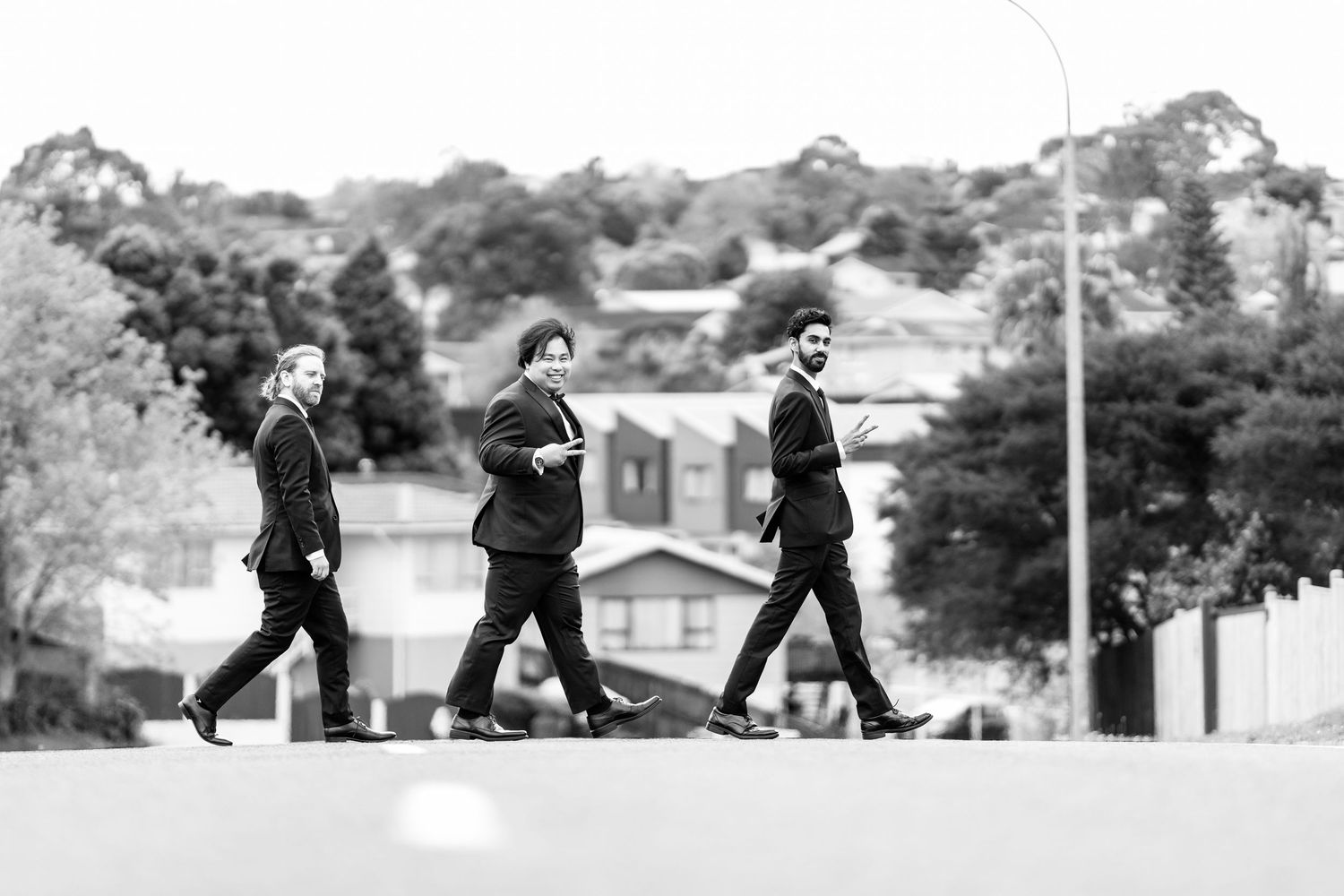 Three people in formal attire walk across a street in black and white photography.