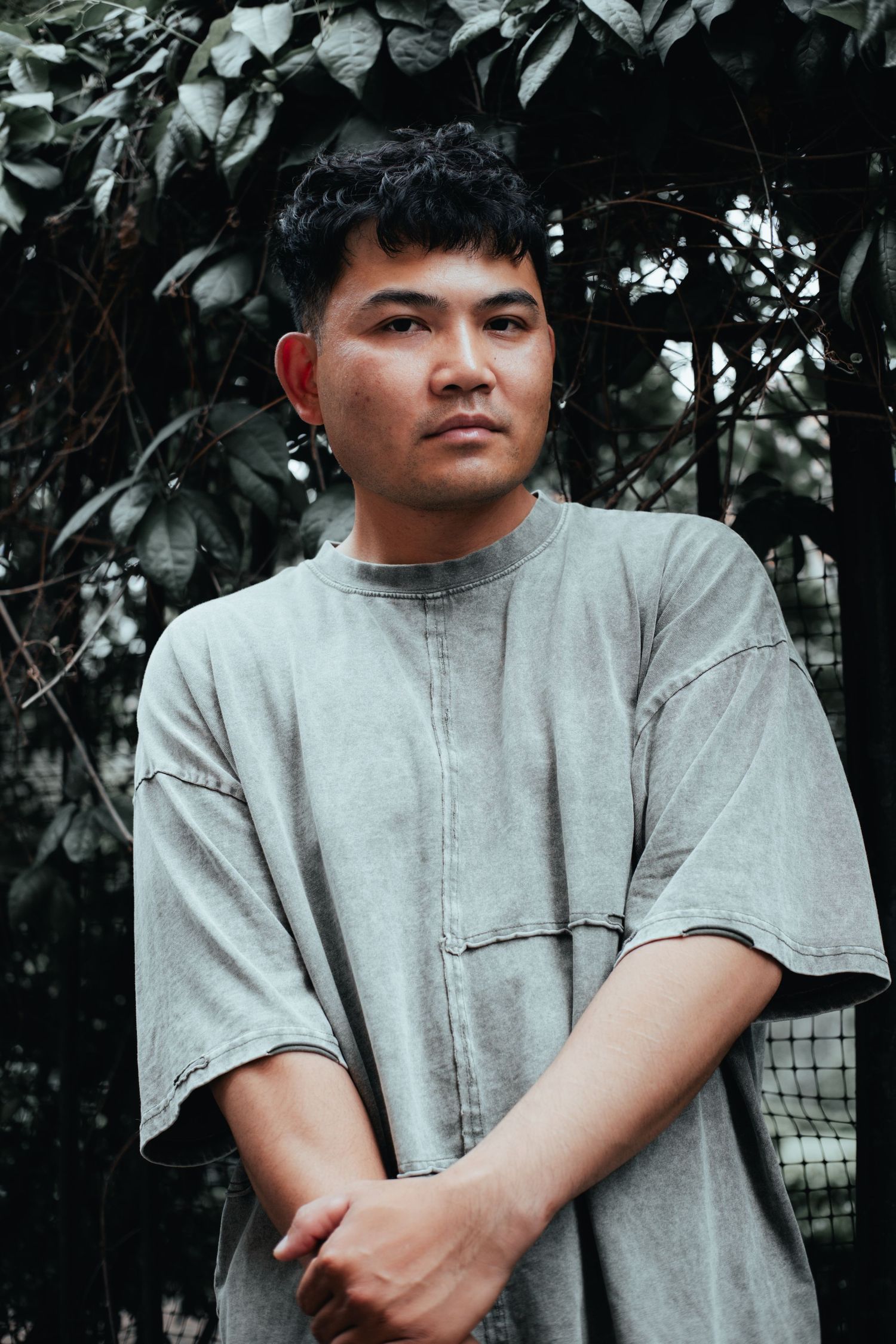Portrait showing someone in grey t-shirt against leafy green background.