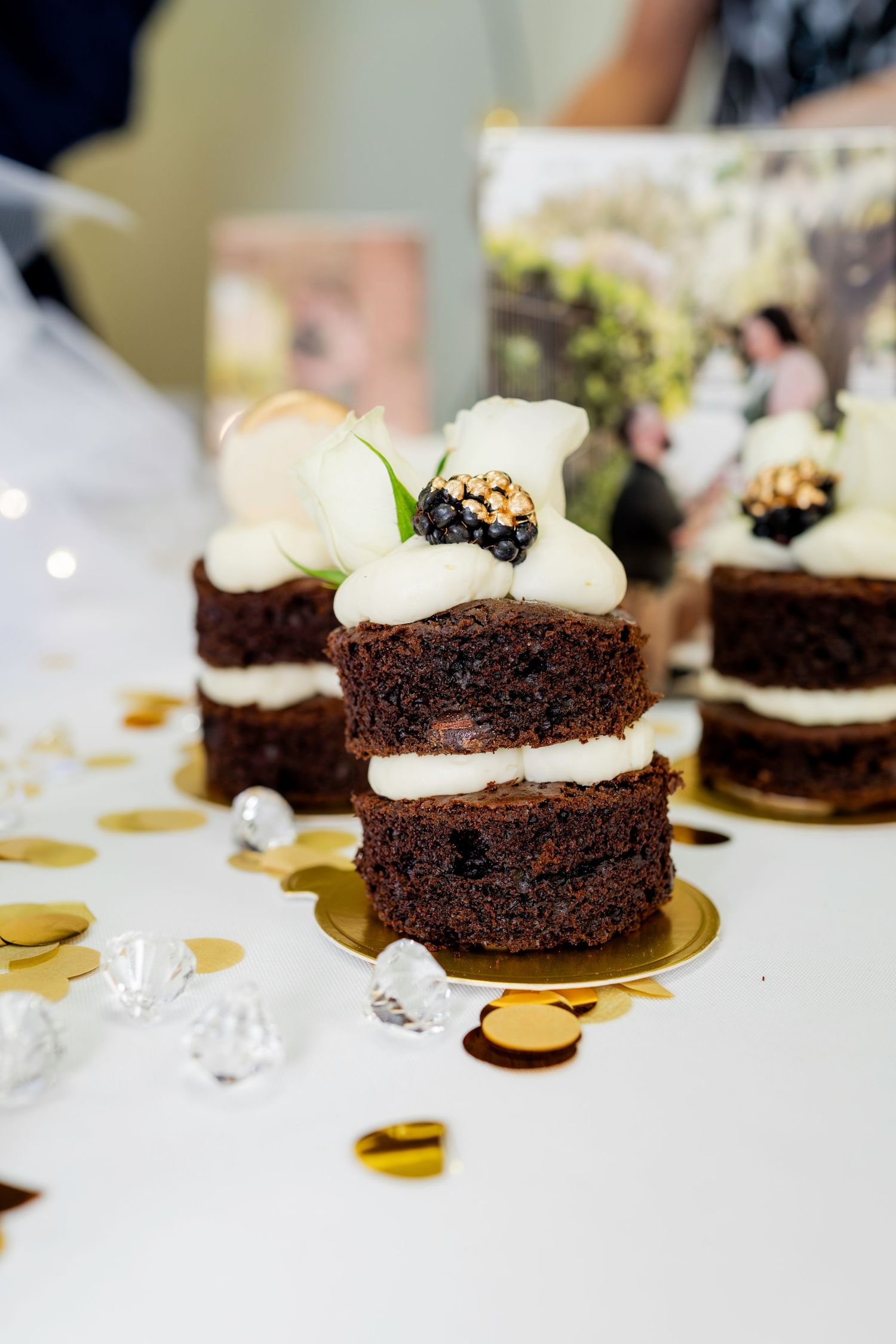 Chocolate mini cakes with white frosting and dark garnish arranged on golden metallic plates.