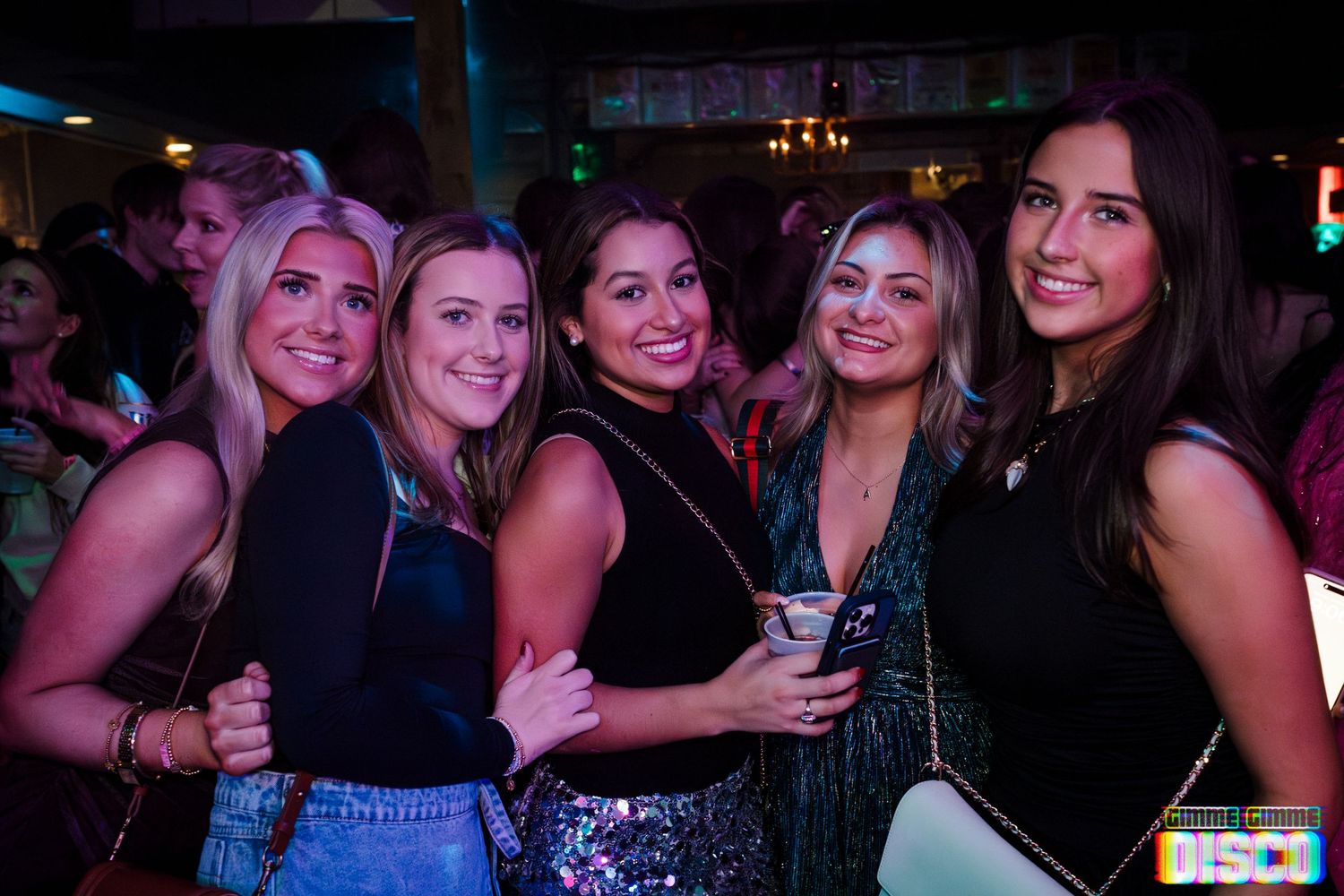 A group poses together at a nightclub event with dark lighting and neon accents.