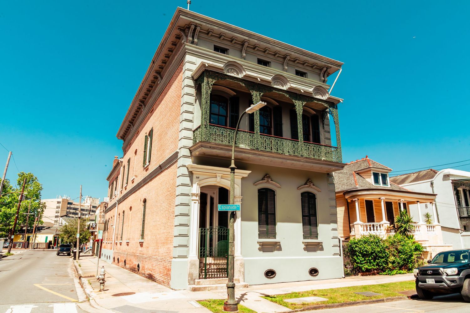 Historic New Orleans corner building with ornate balcony and quoined facade stands against bright blue sky in residential area.