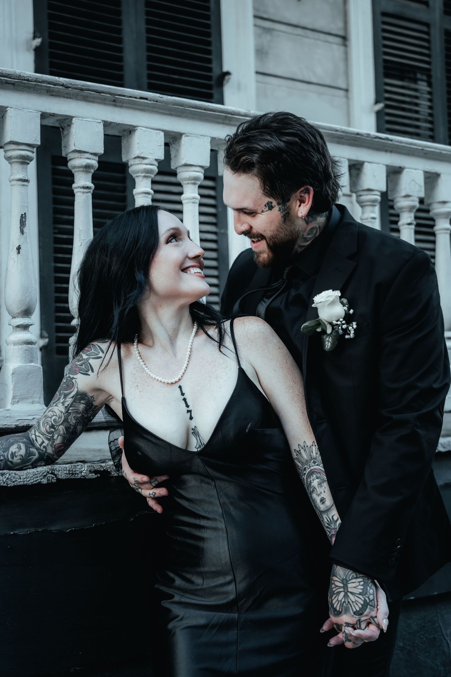 A couple in black attire sharing a romantic moment together in front of a white architectural backdrop.