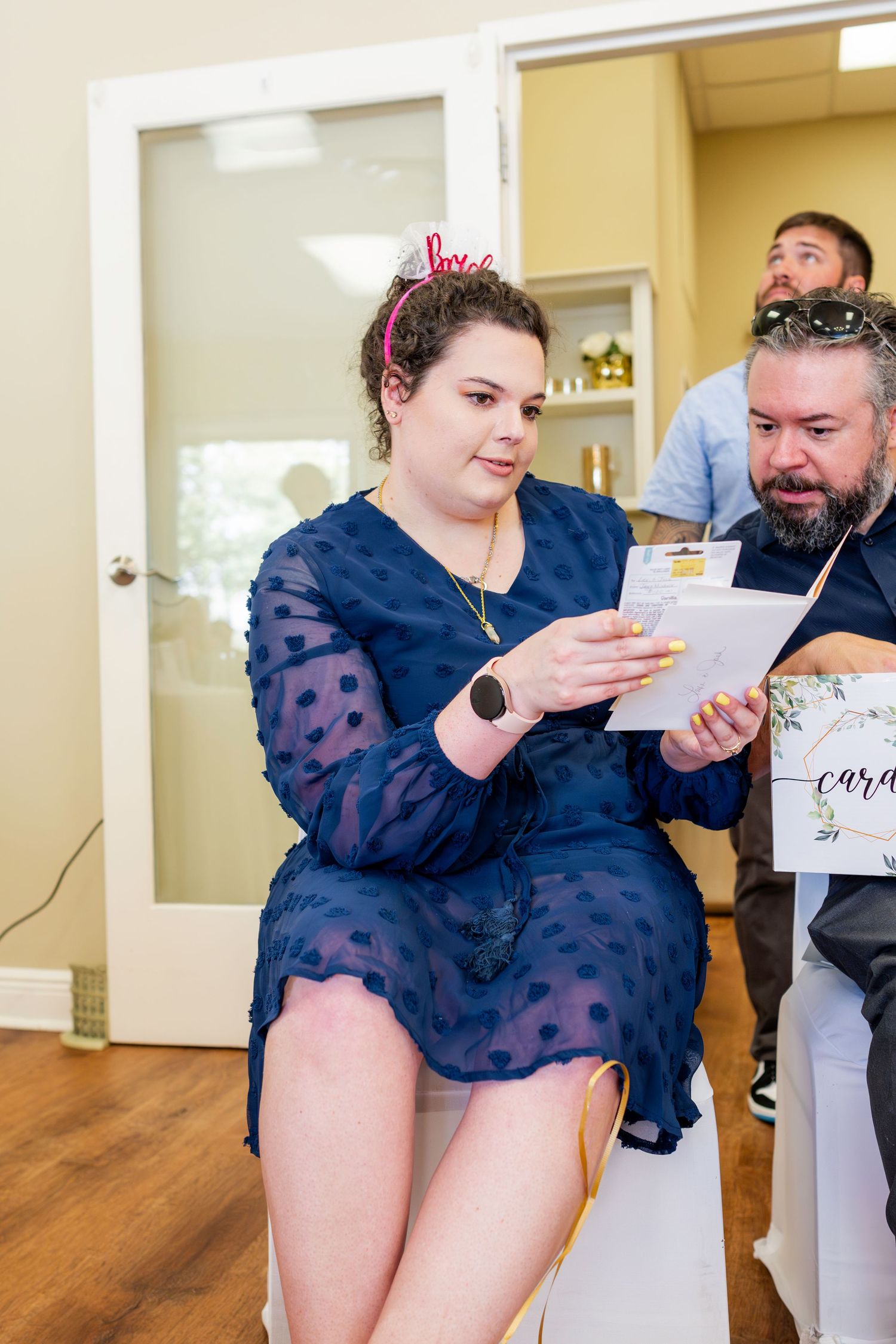 Guest in navy blue polka dot dress reads a card at special event with balloon decorations.