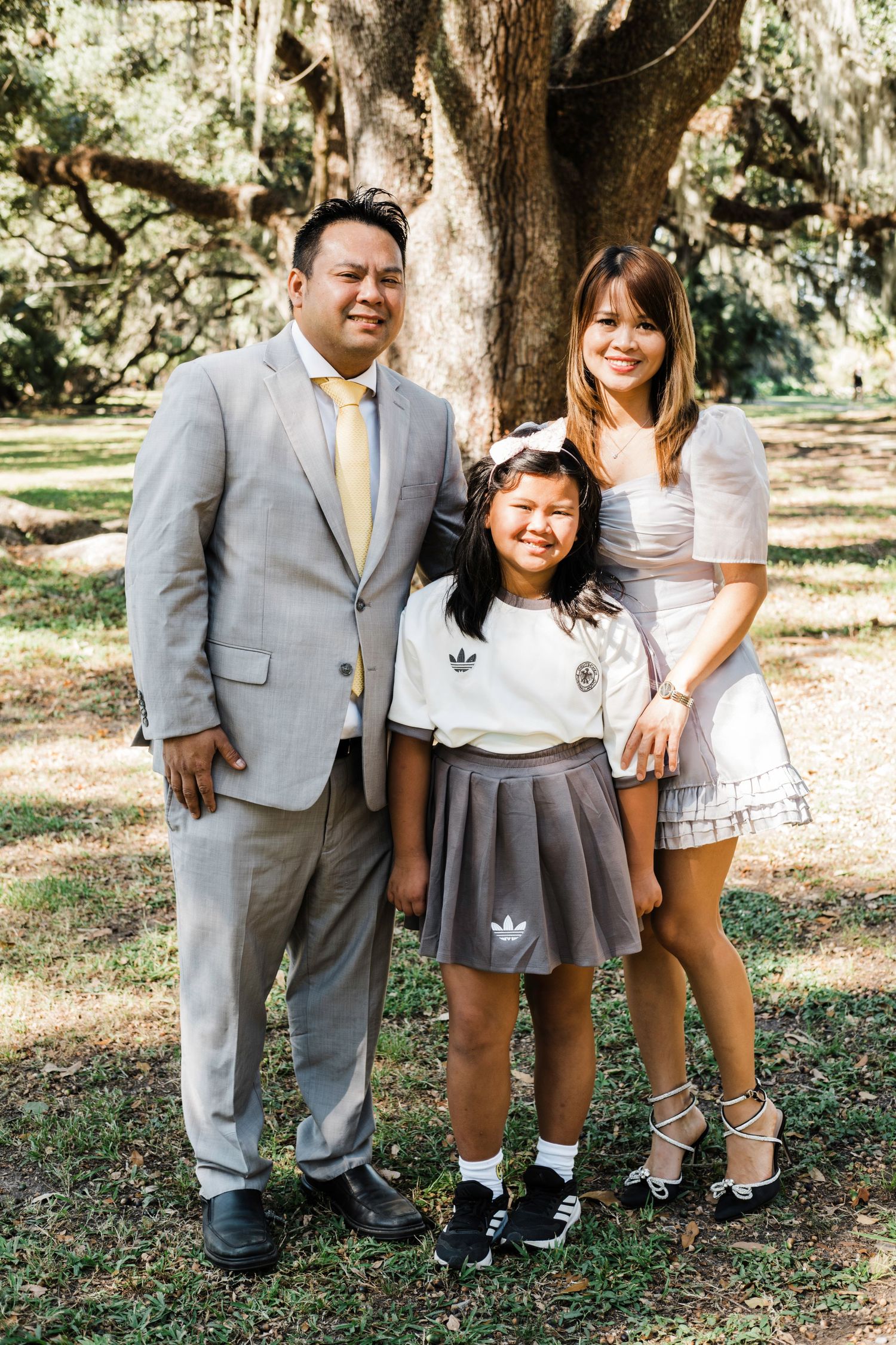 A family in formal attire poses together under a tree in a park setting.