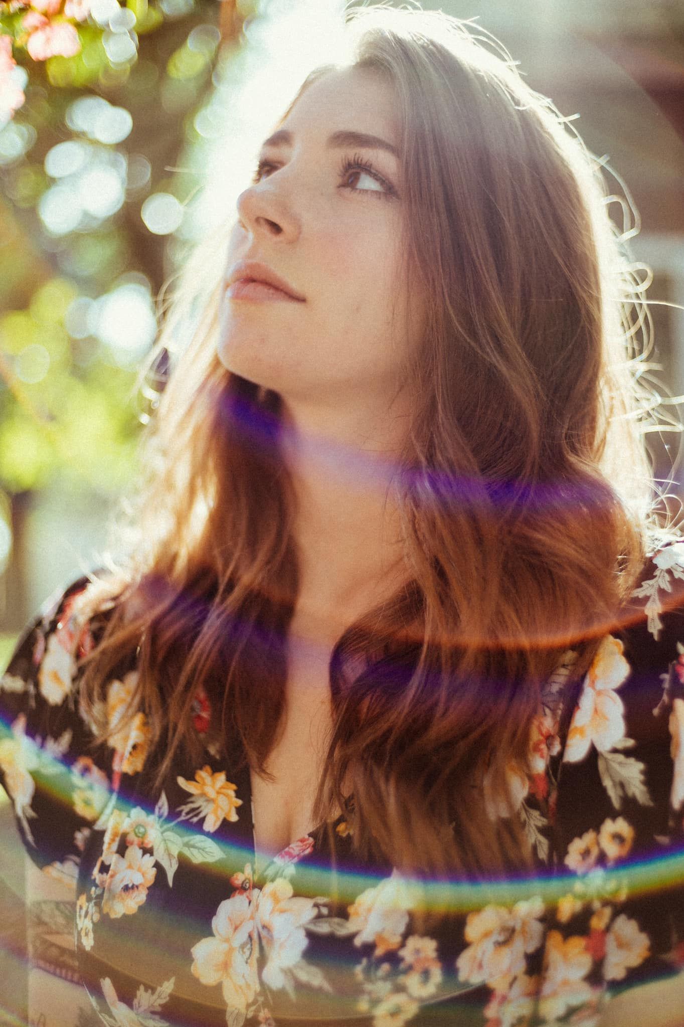 Portrait photo with sunlit bokeh and lens flares, wearing a floral print dress against a soft natural background.