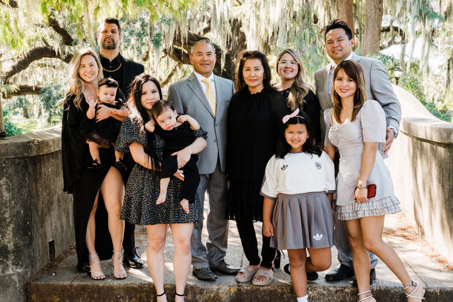 Extended family gathering poses together under Spanish moss trees in coordinated formal attire.