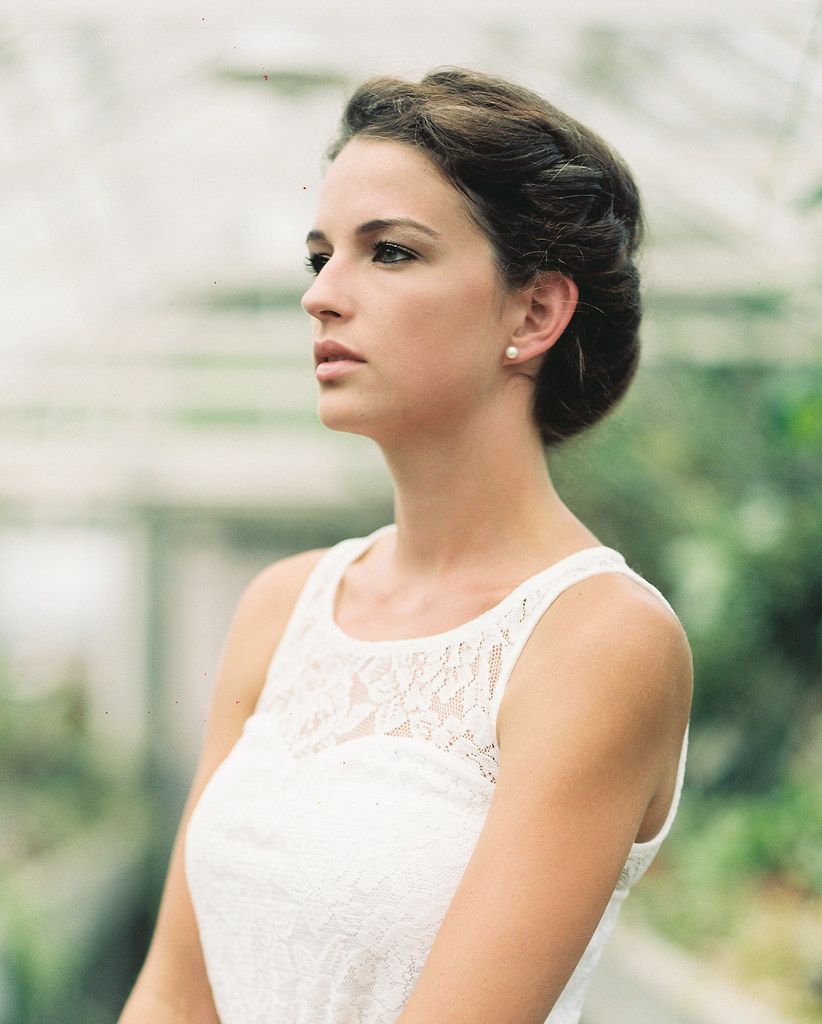 Elegant bride in white lace dress poses outdoors with classic updo hairstyle.