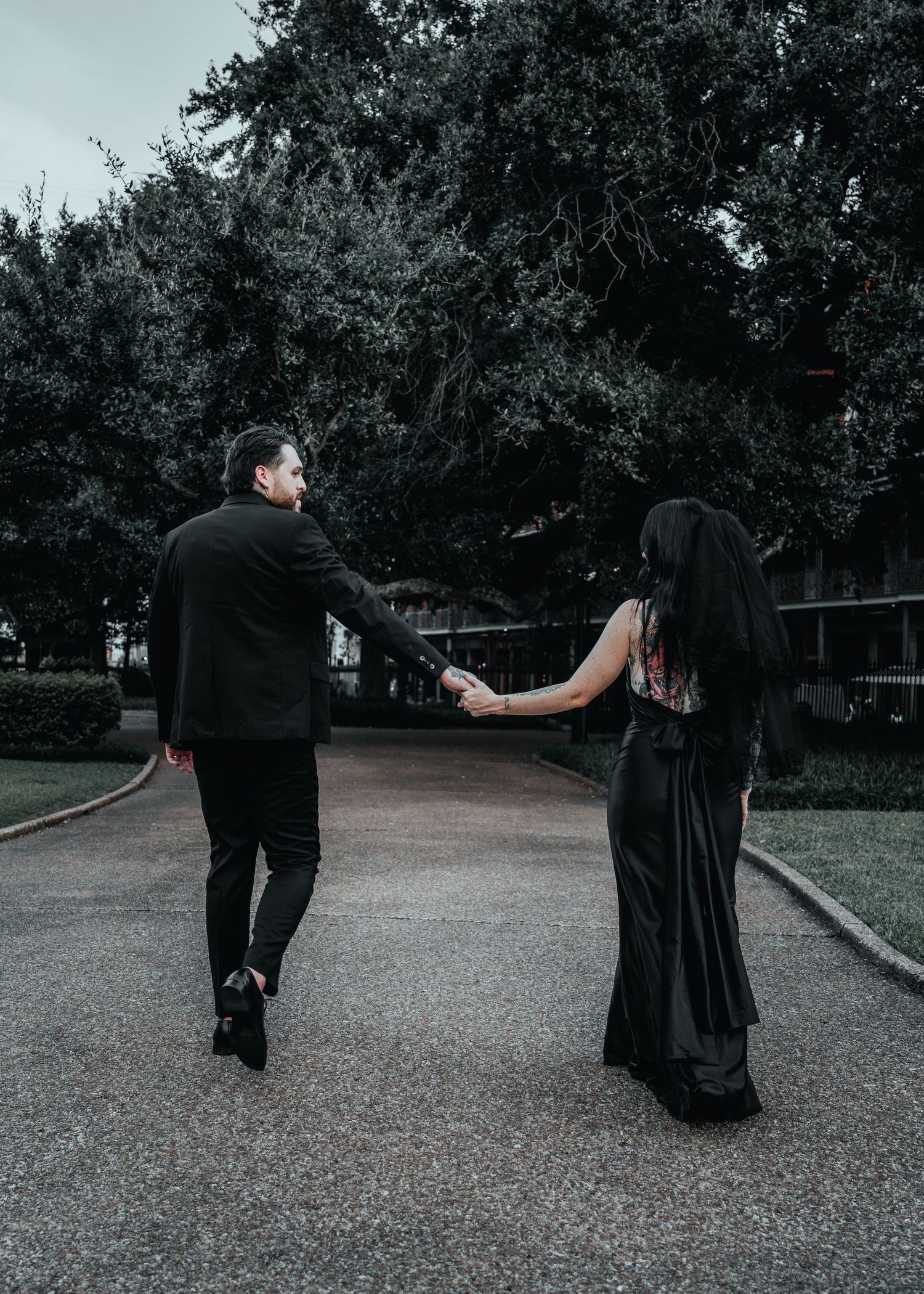 Person in dark attire walking through park pathway performing artistic movement sequence.