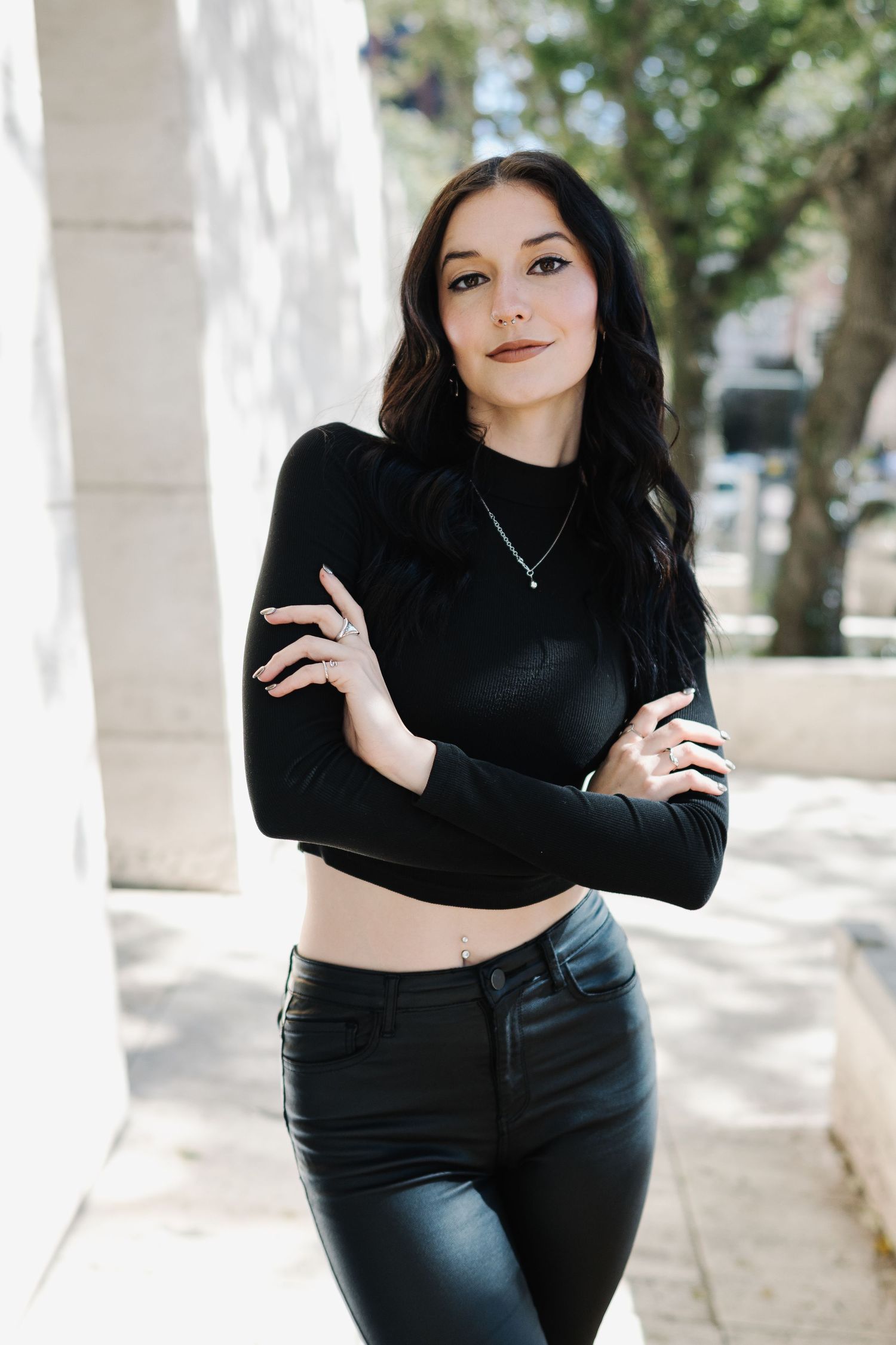 Fashion portrait in black crop top and leather pants against white column outdoors.