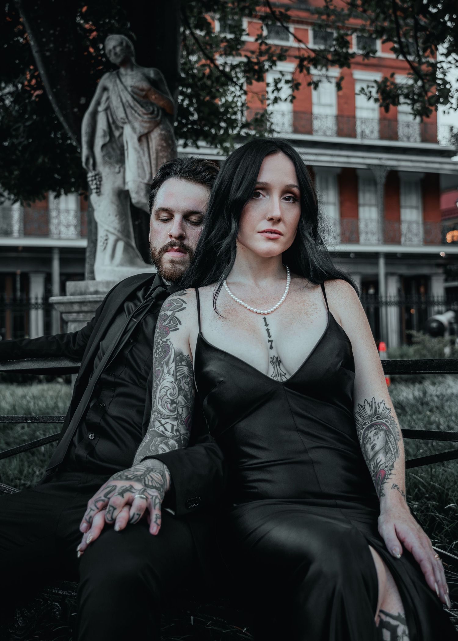 Moody gothic couple in black attire pose together on stone steps with a classical statue in New Orleans French Quarter.