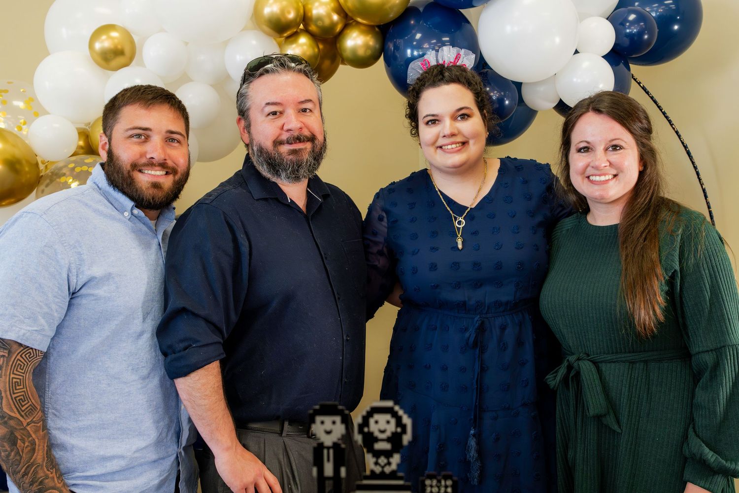 Group photo at a celebration with navy blue and gold balloon decorations in the background.
