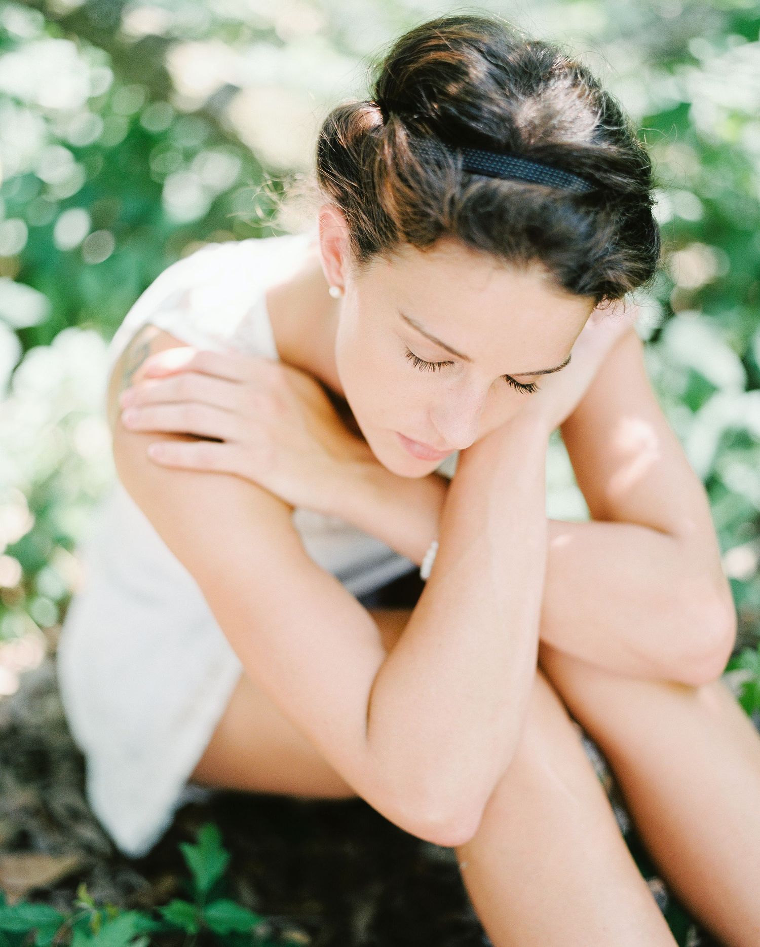 Soft portrait of someone in a delicate pose with eyes closed against a dreamy green bokeh background.