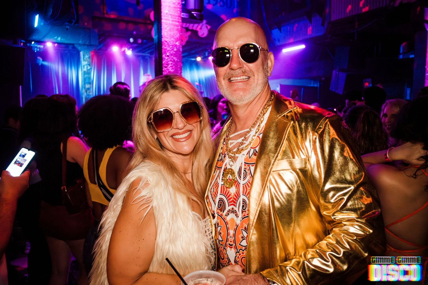 Party-goers in retro disco outfits and sunglasses pose at a nightclub event.