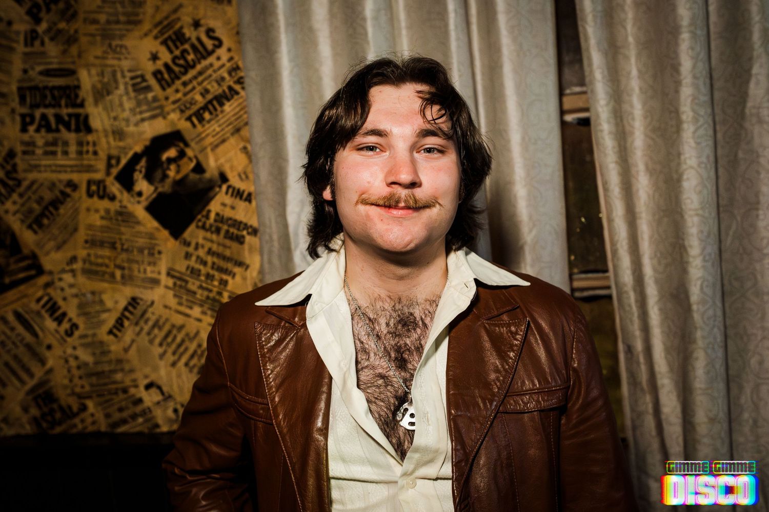 Portrait of someone in a leather jacket against a wall covered in vintage posters.