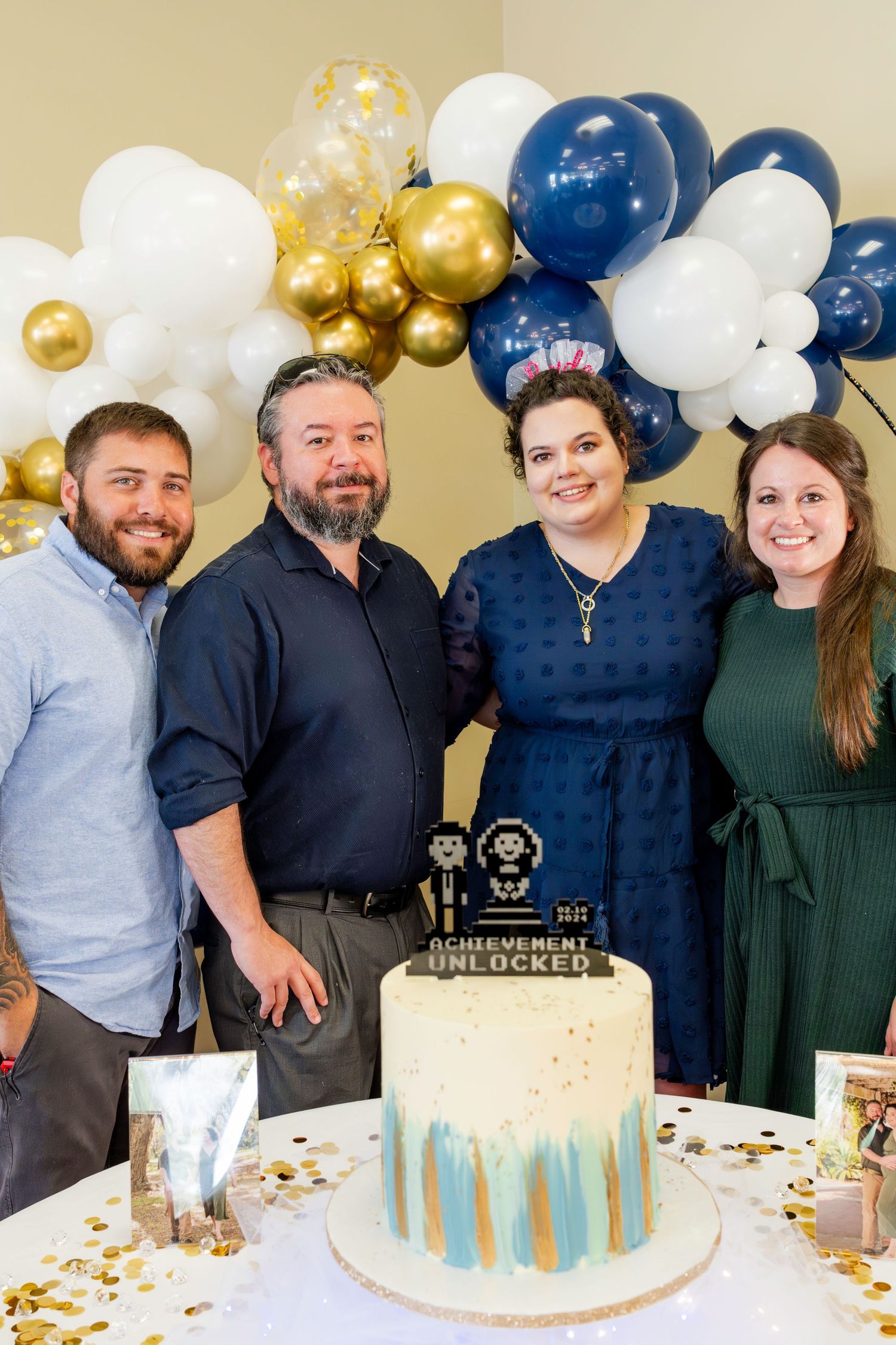 A celebration with a white and blue cake decorated with gold accents, surrounded by festive blue and gold balloons.