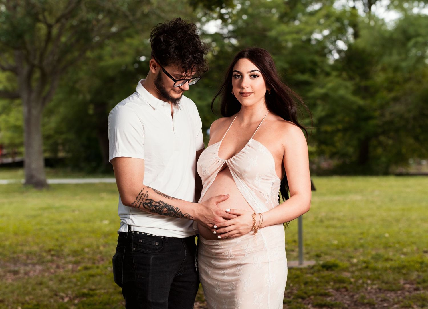 Romantic maternity photo of couple embracing in park setting.