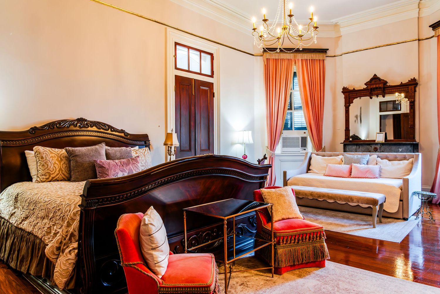 Luxurious period bedroom featuring dark wood furniture, coral drapes, and ornate decor in warm lighting.