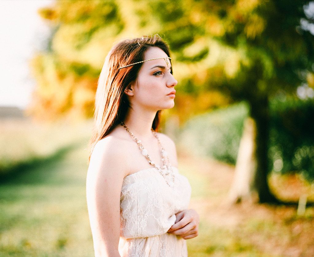 A serene figure in a white flowing dress stands gracefully in a golden autumn field during sunset.