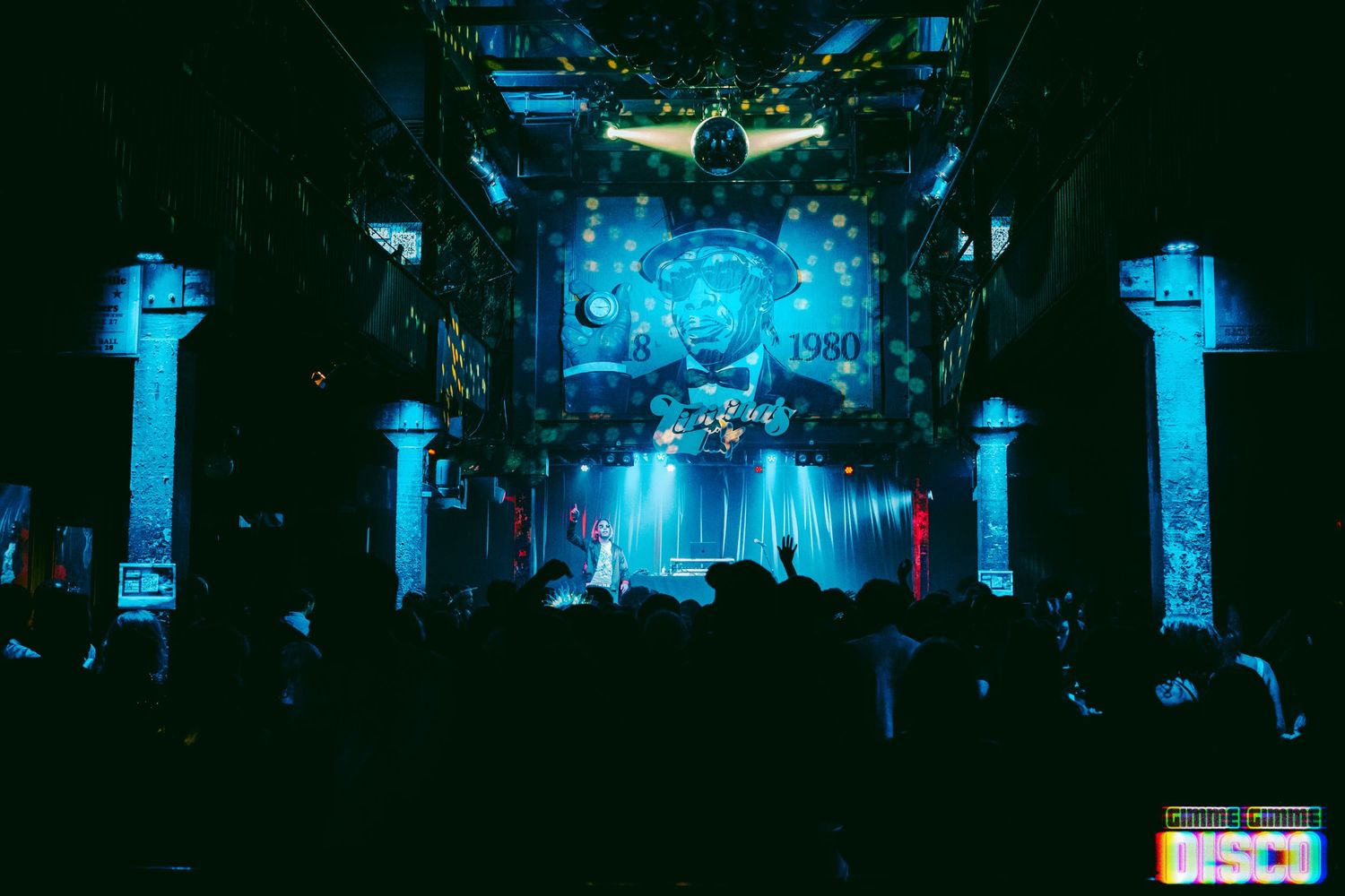Blue lights illuminate a nightclub interior with classical columns and an ornate ceiling.