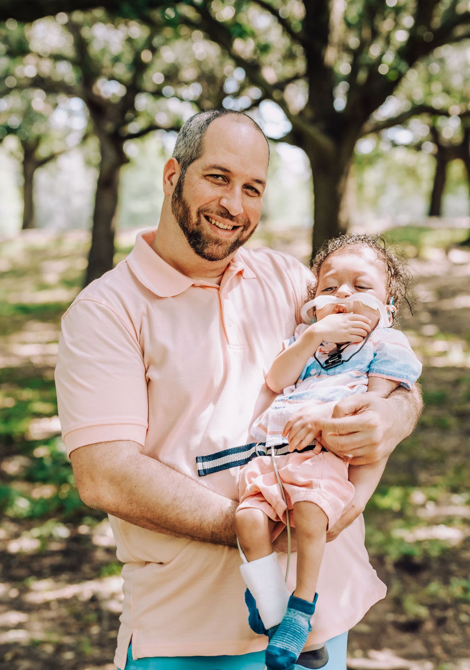 A parent and young child sharing a joyful outdoor moment together under dappled sunlight and trees.