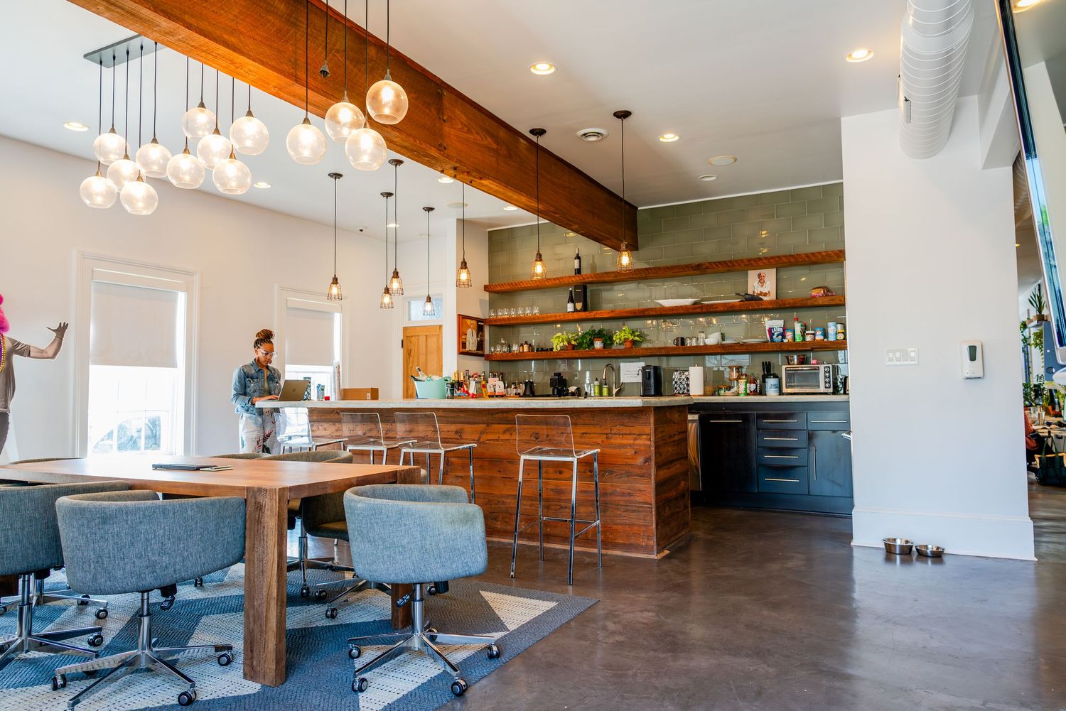 Modern restaurant bar interior with hanging glass pendant lights, blue barstools and wooden accents throughout the space.