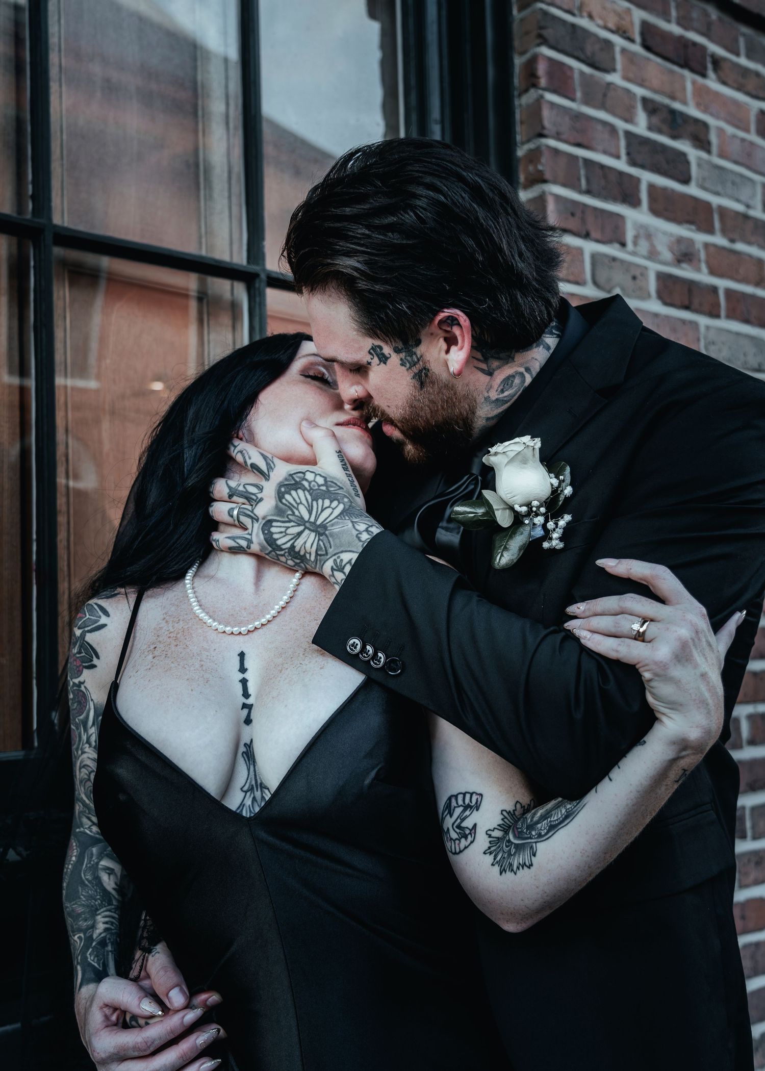 Romantic photo series showing a couple in black clothing sharing intimate moments against a brick wall backdrop.