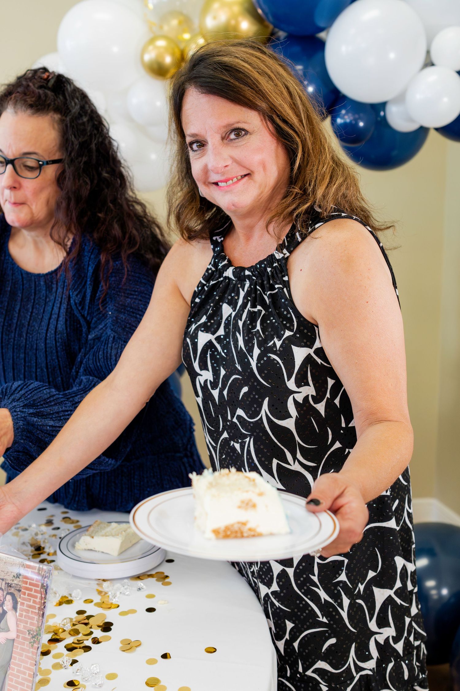 Elegant party scene with navy and gold balloon decorations as guests serve cake at a celebration.