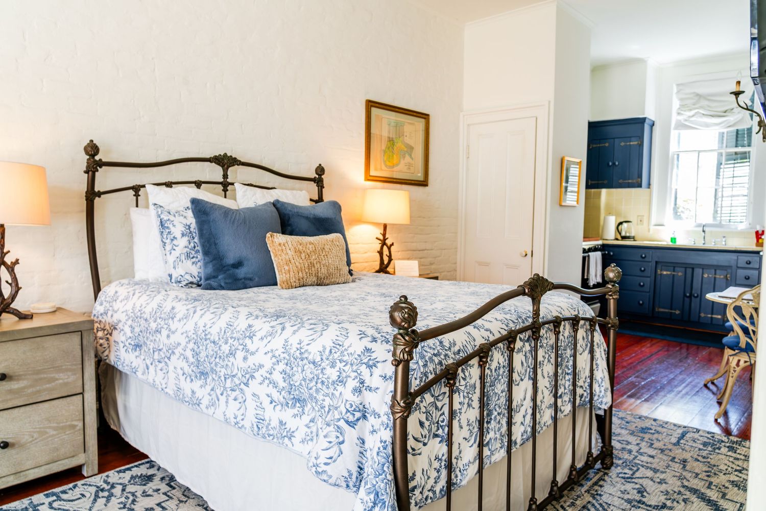 Cozy bedroom with wrought iron bed frame, blue and white floral bedding, and vintage-style nightstand in bright space.