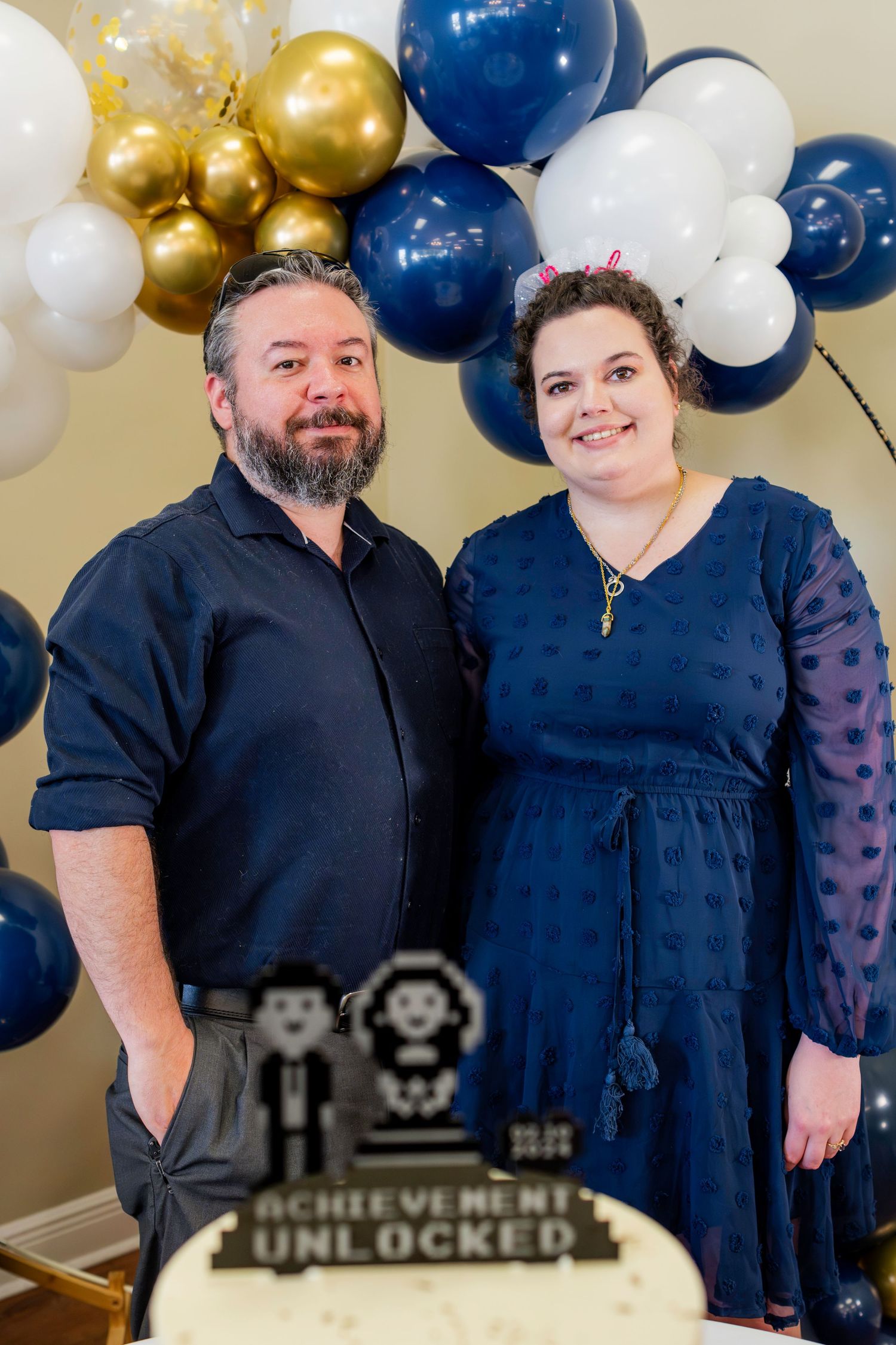 Celebration backdrop with gold and navy balloon arch and video game achievement decor.