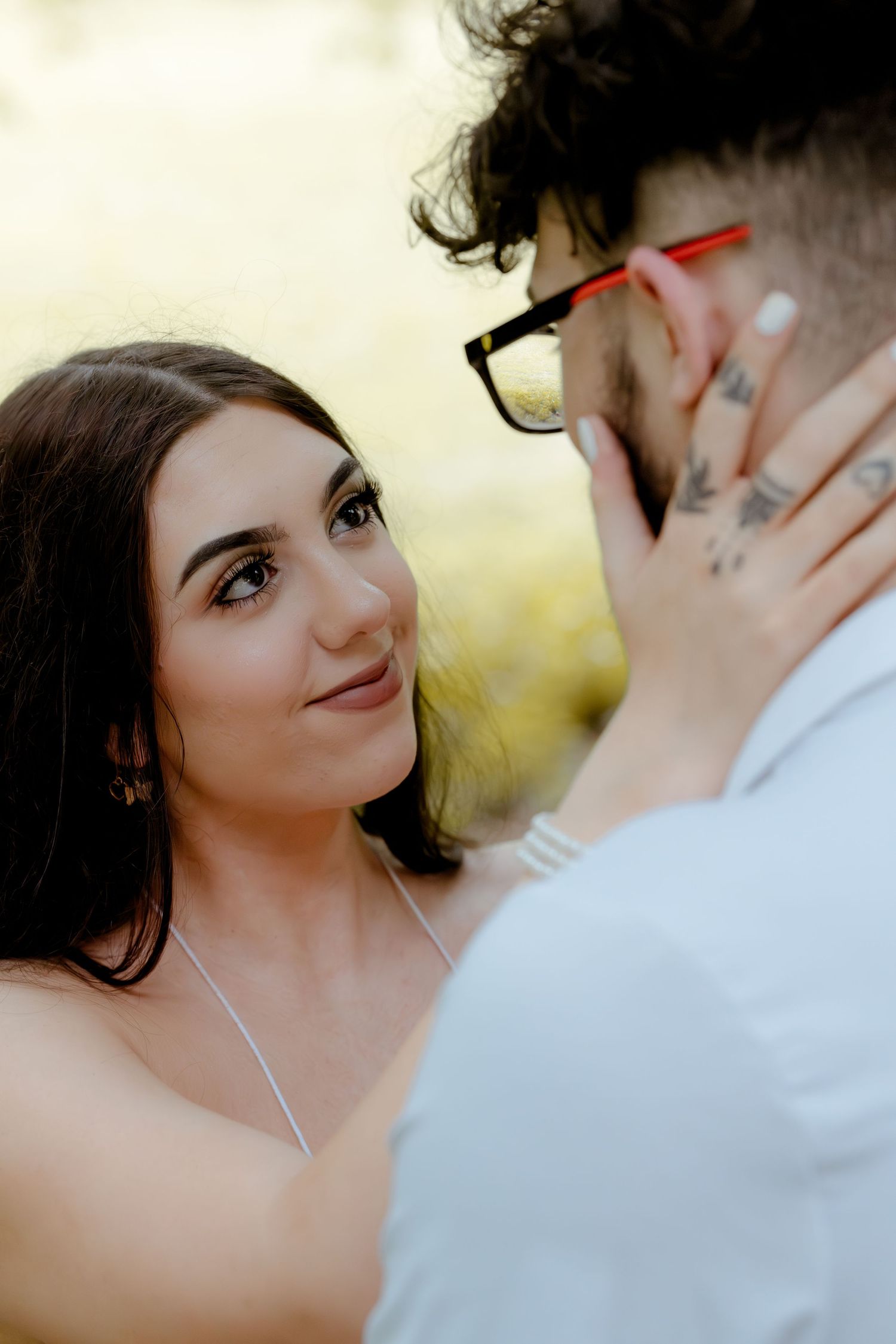 A romantic couple shares an intimate moment outdoors with the woman gently touching her partner's face in soft lighting.