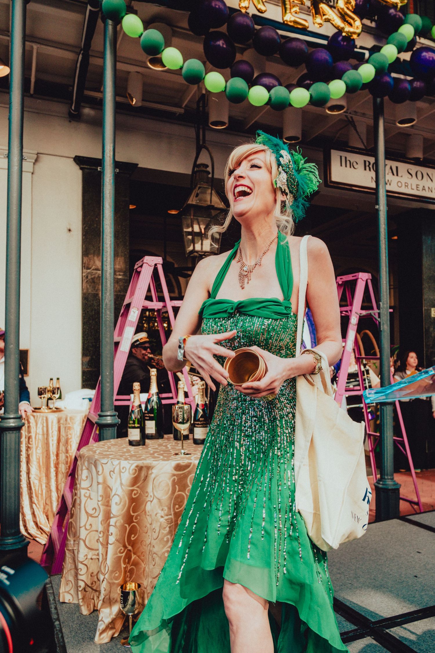 Woman in sparkling green dress and matching headpiece celebrating at Mardi Gras street party.
