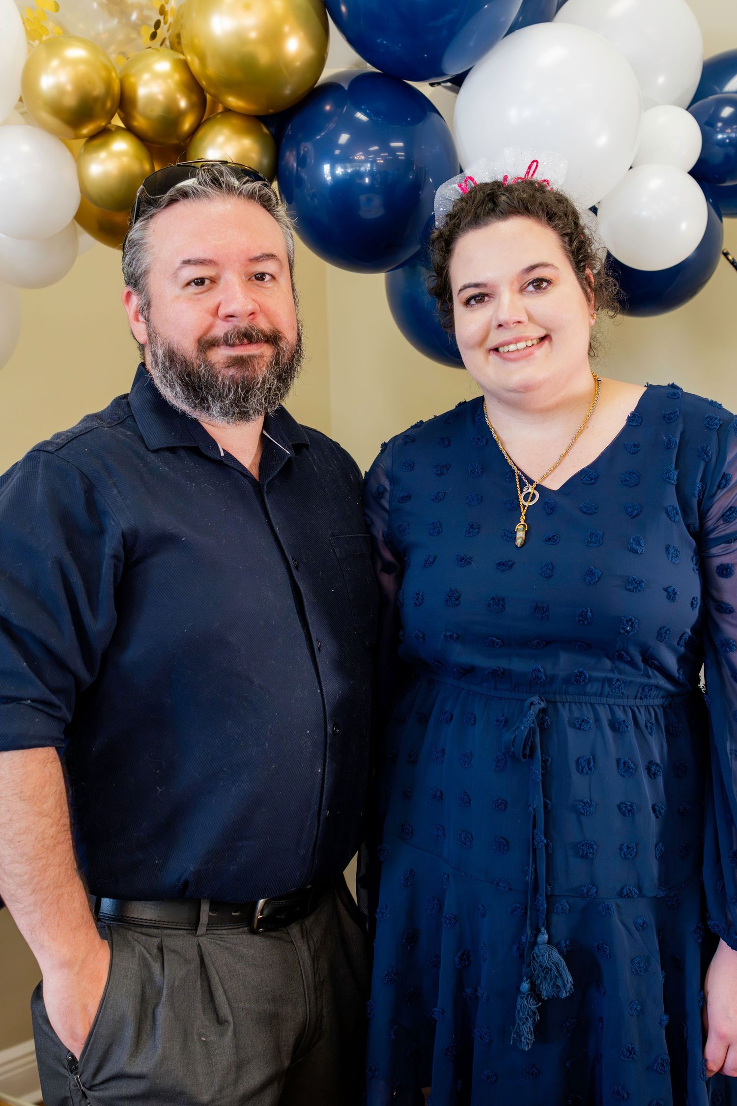 Navy blue and gold themed celebration portrait with balloon arch backdrop.