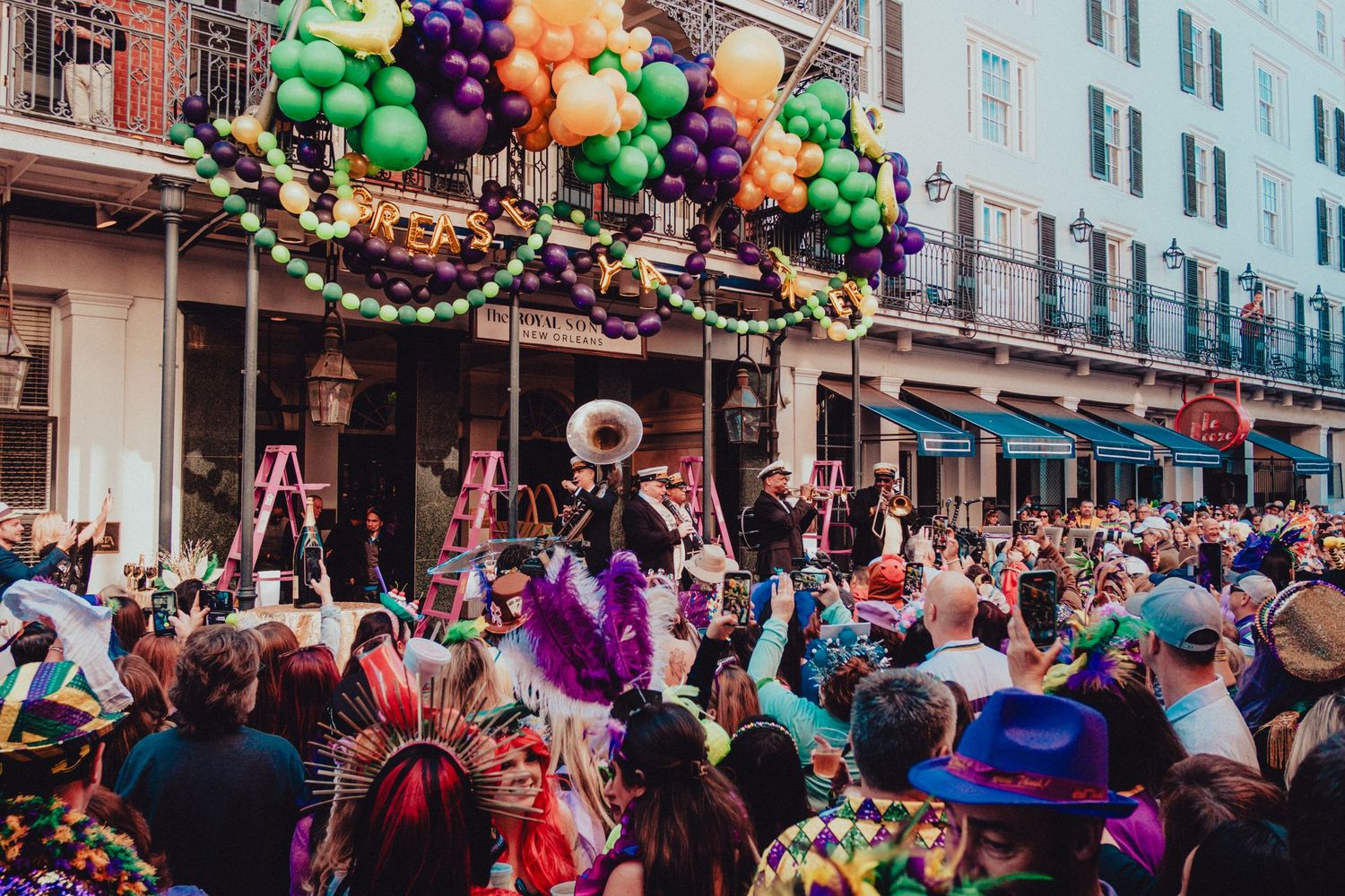 Vibrant street celebration with rainbow balloon arch and costumed revelers in the French Quarter.