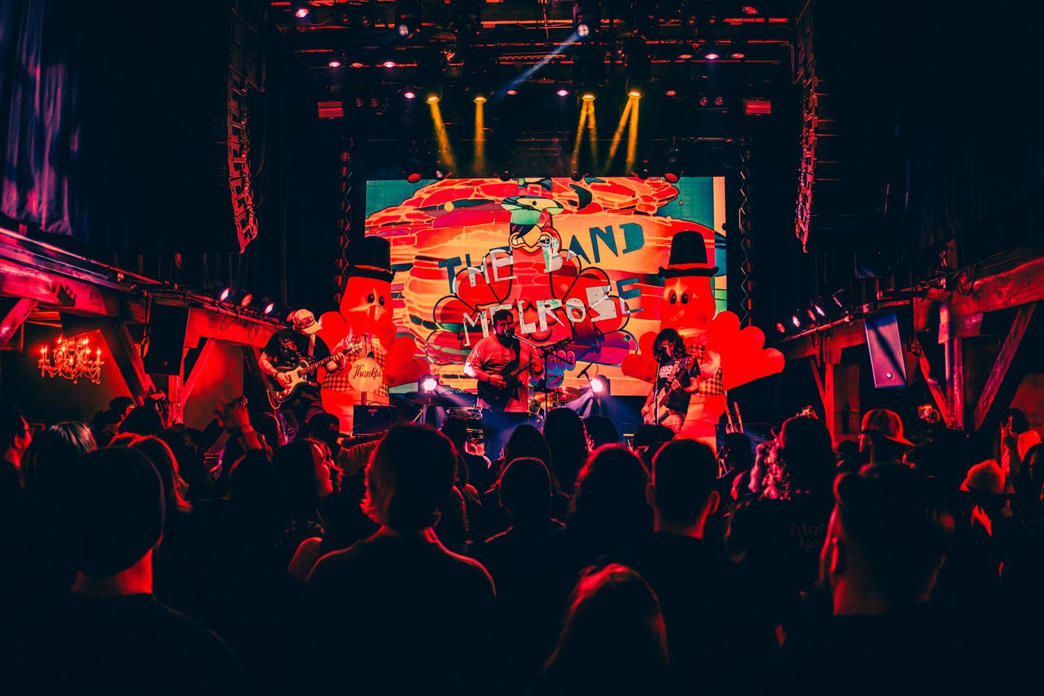 Concert crowd silhouetted against red stage lighting with bright LED screen display.