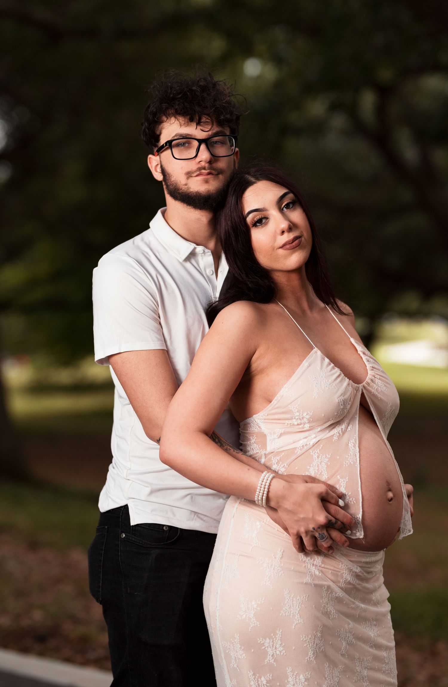 An expectant couple embraces in romantic outdoor maternity portrait with soft lighting.