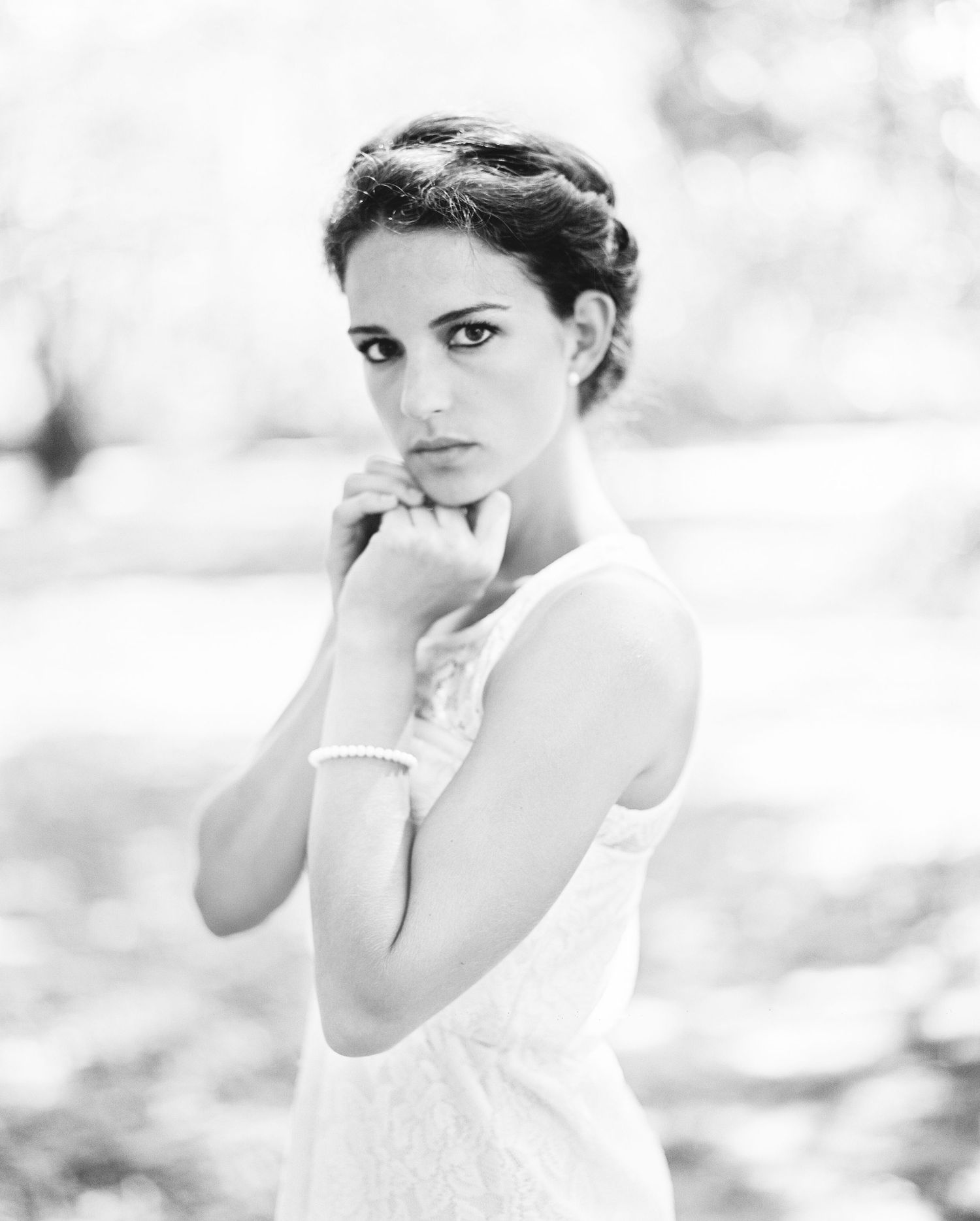 Black and white romantic portrait showing an elegant woman in white dress and pearl bracelet, posed outdoors.