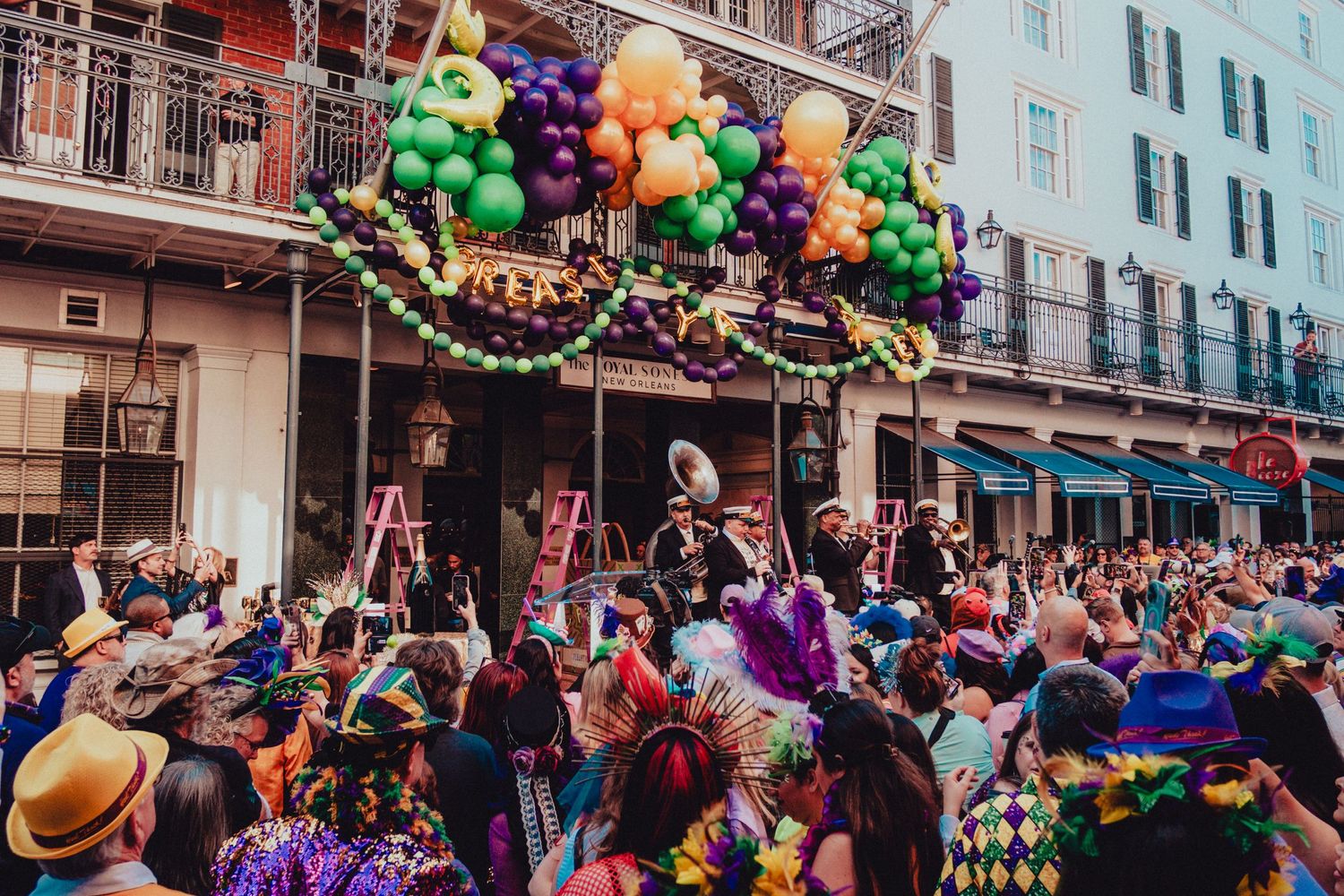 Colorful Mardi Gras celebration in New Orleans French Quarter with balloon decorations and festive crowd.